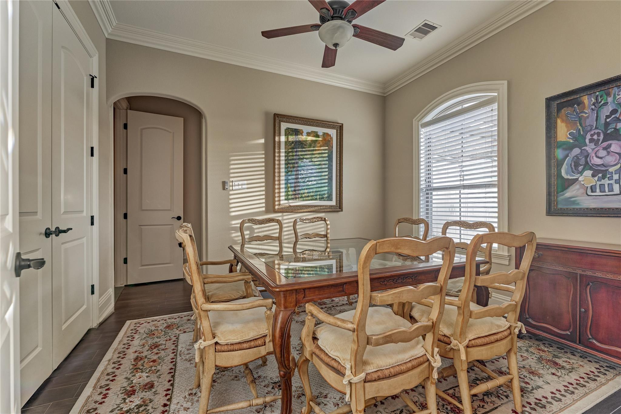 Dining room with a glass-top table, carved wooden chairs, and an arched window with blinds.