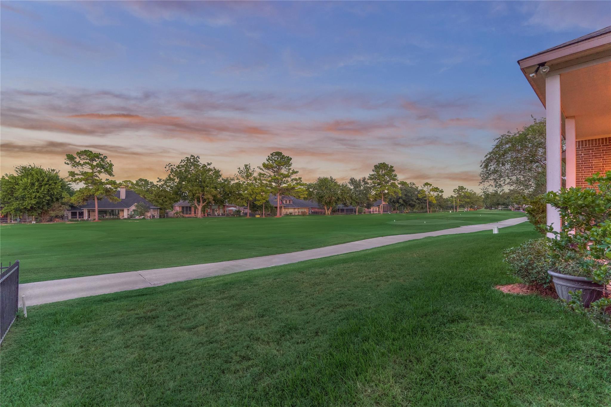 Golf course lawn and paved path beside a brick home at sunset.