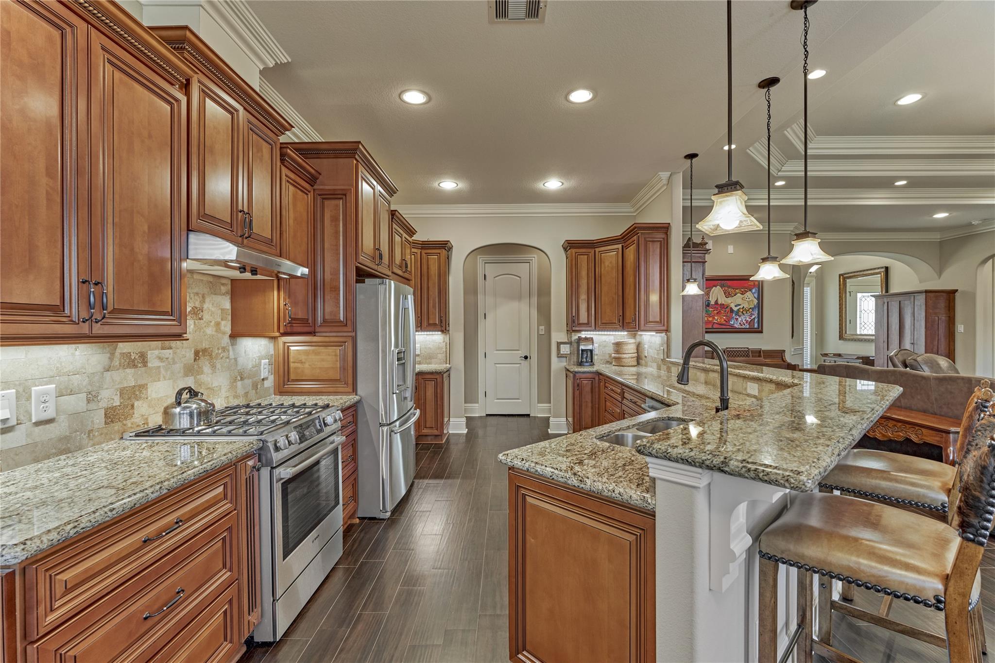 Kitchen with dark wood cabinets, granite island, stainless steel appliances, and pendant lighting.