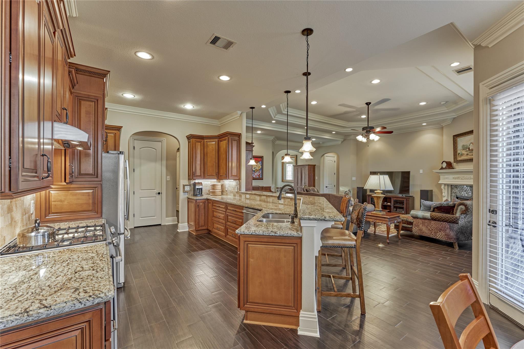 Kitchen with wood cabinetry and granite island opening to a furnished living room with fireplace.