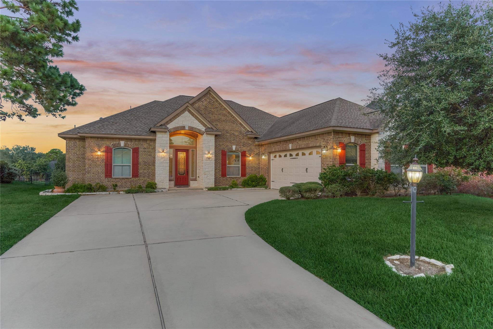 Brick home with stone entry, red shutters, two-car garage, and curved driveway at dusk.