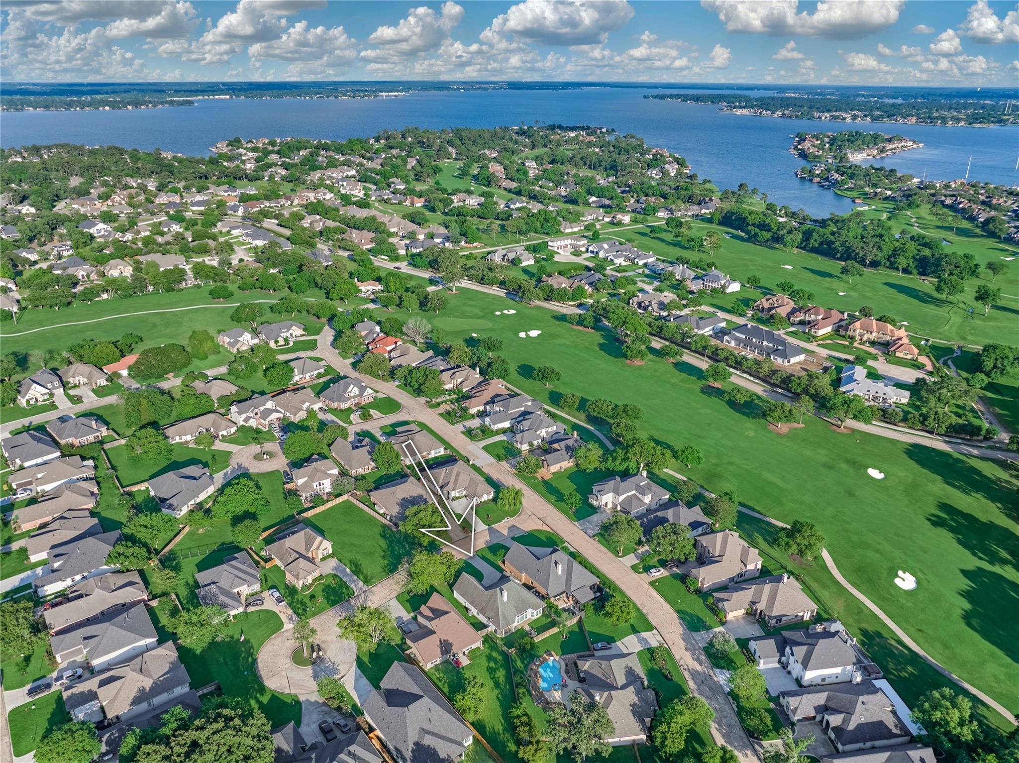 Aerial view of a lakeside neighborhood and golf course, with an arrow marking the property.