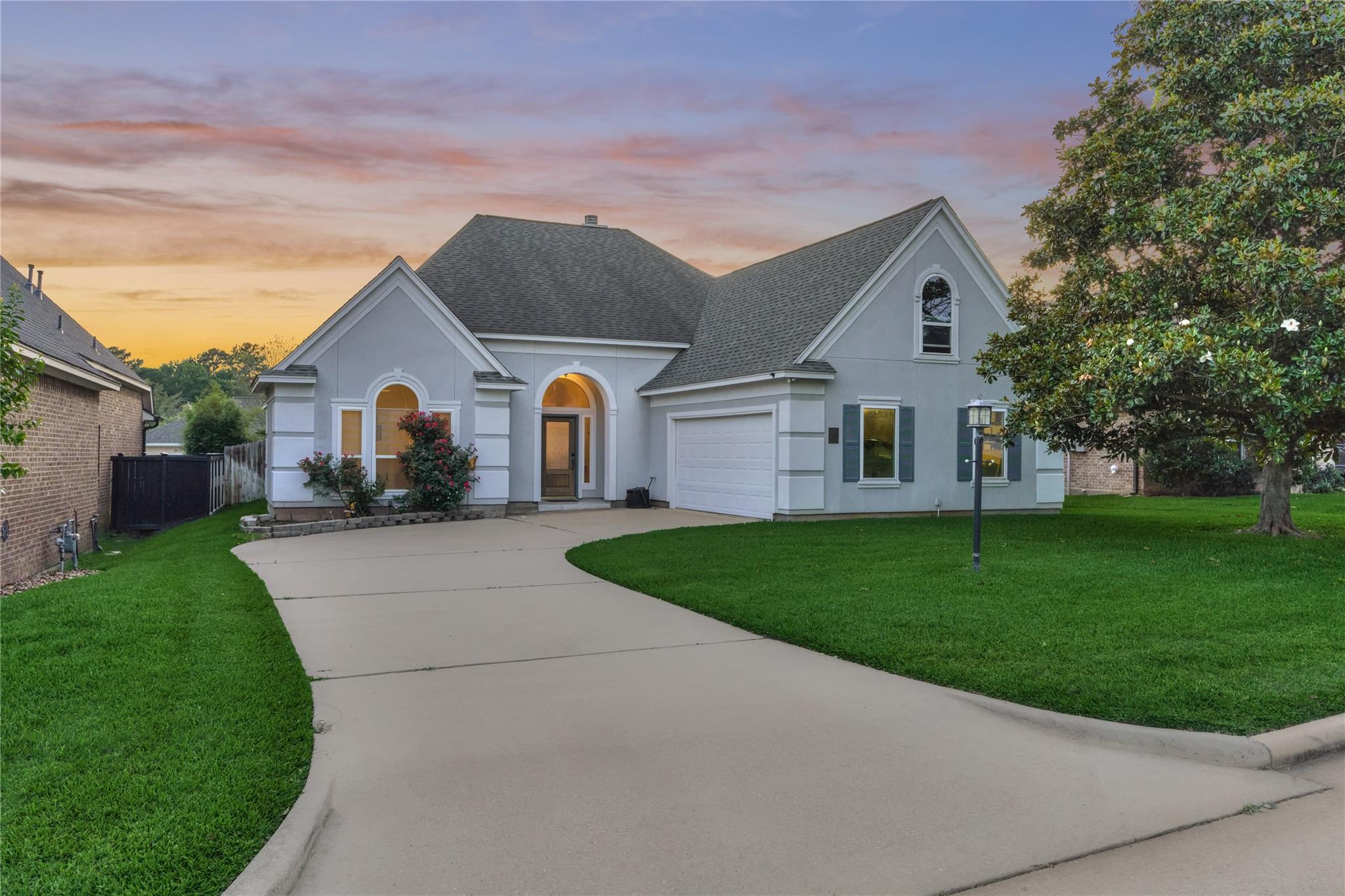 Light gray gabled house with an arched entry and curved driveway at sunset.
