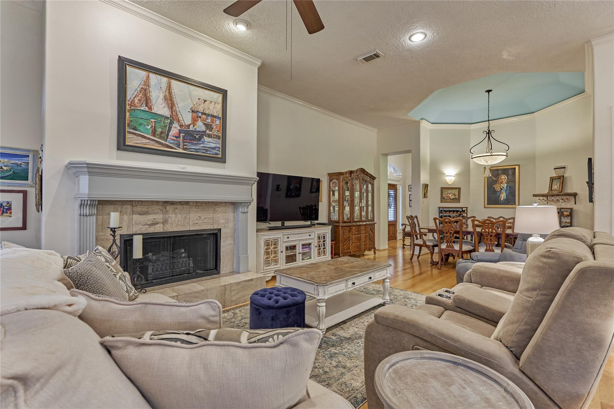 Living room with a stone fireplace and an adjoining dining area beneath a raised ceiling.