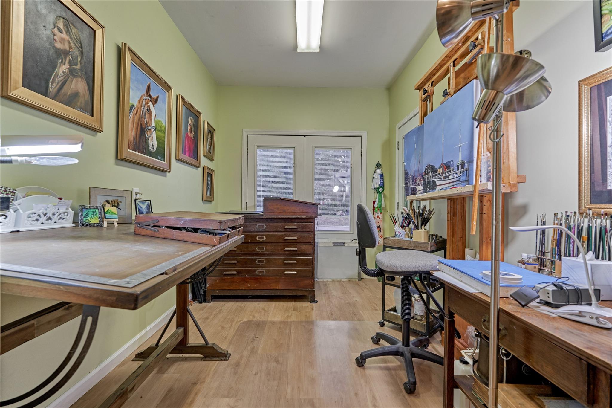 Art studio with wooden worktables, a drafting easel, framed artwork, and art supplies.