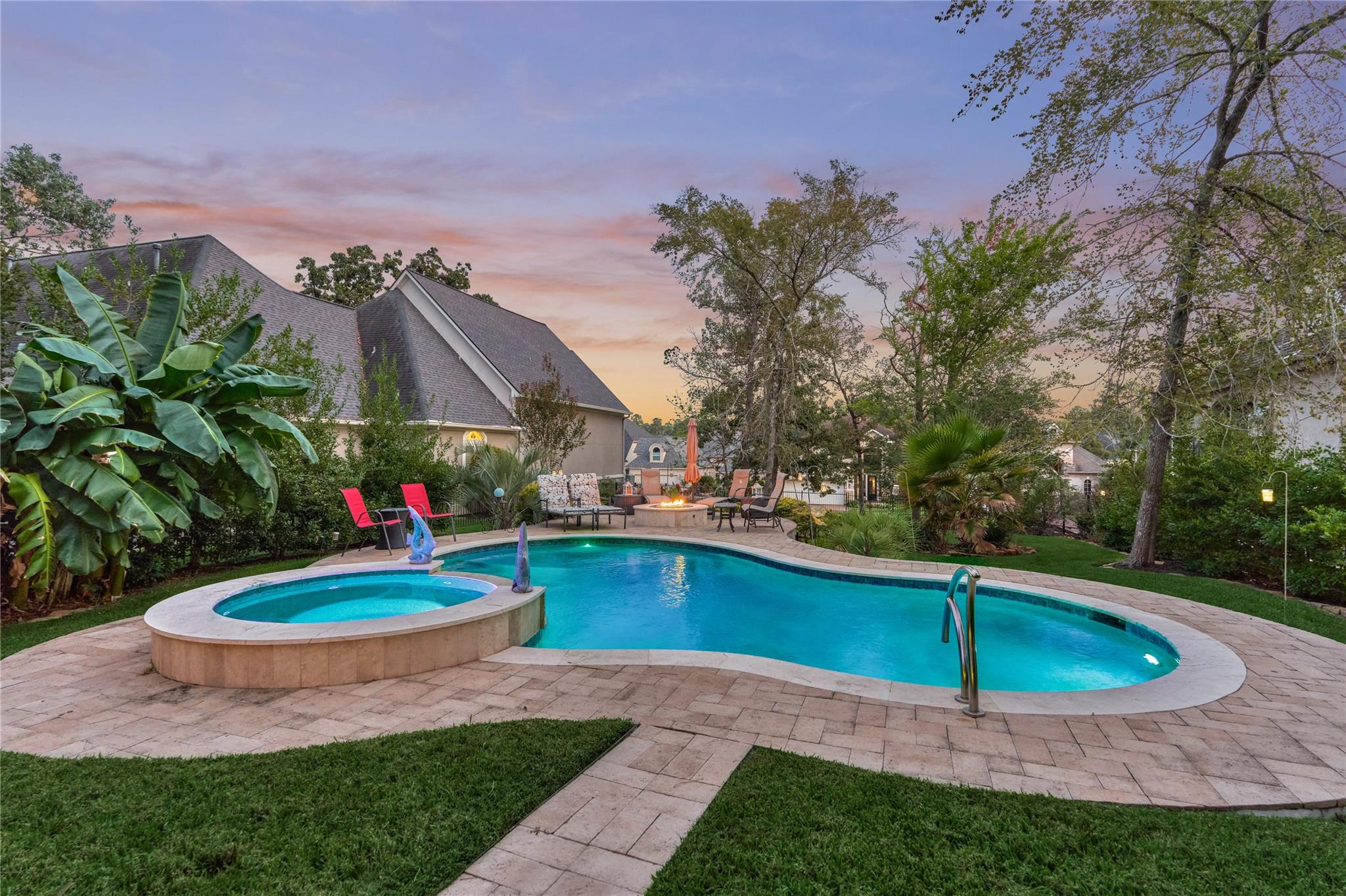 Backyard pool and raised spa with a stone patio, lounge chairs, and fire pit at dusk