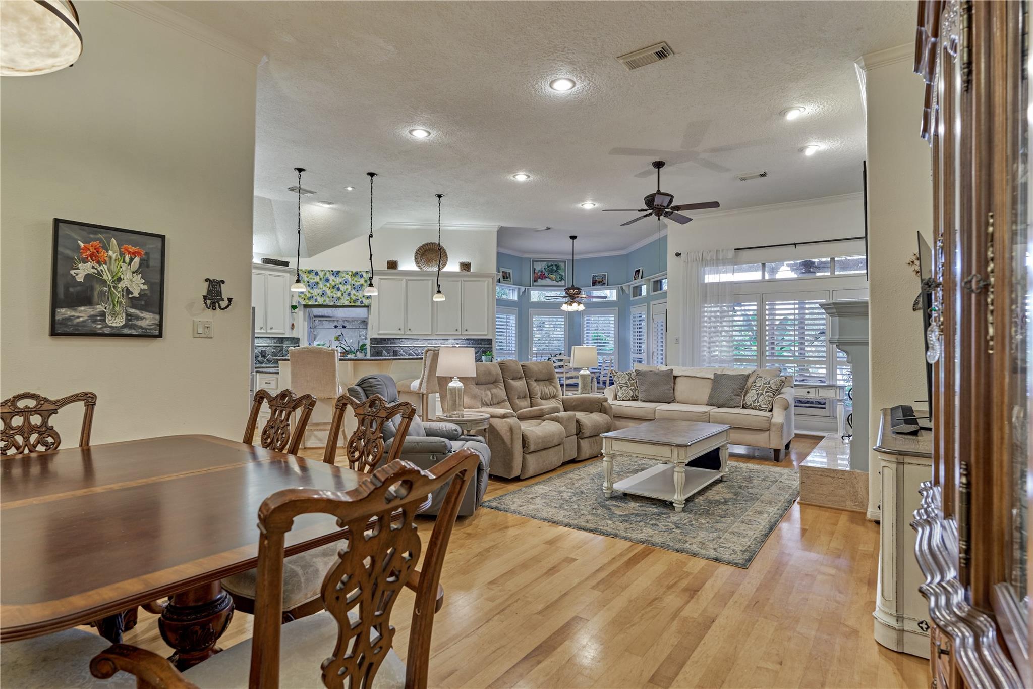 Open-plan living and dining room with light wood floors, a dining table, and a seating area by shuttered windows.