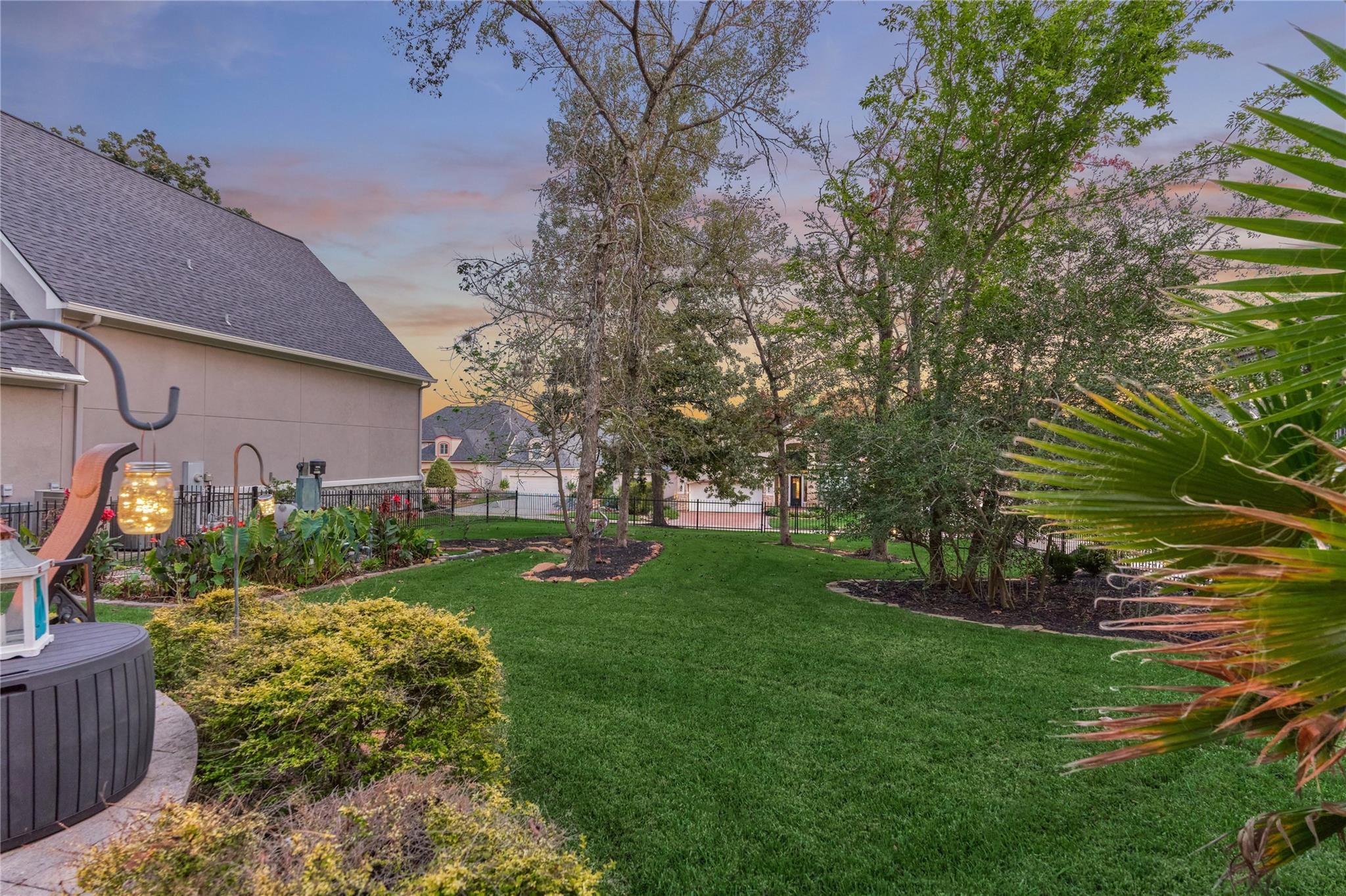 Landscaped backyard with a wide lawn, mature trees, and a hot tub beside the house.