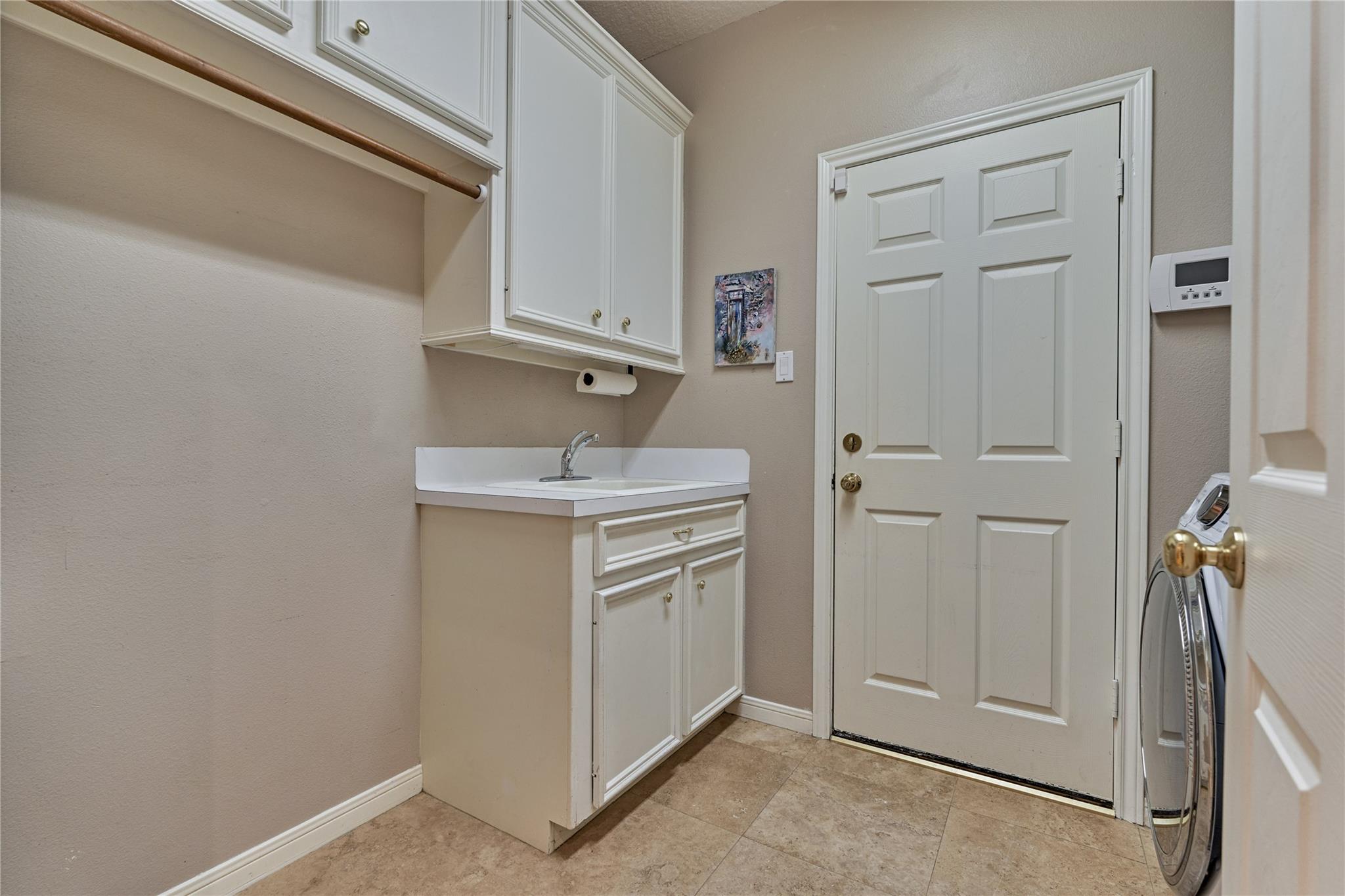 Laundry room with a utility sink, white cabinets, and a partially visible front-loading washer.