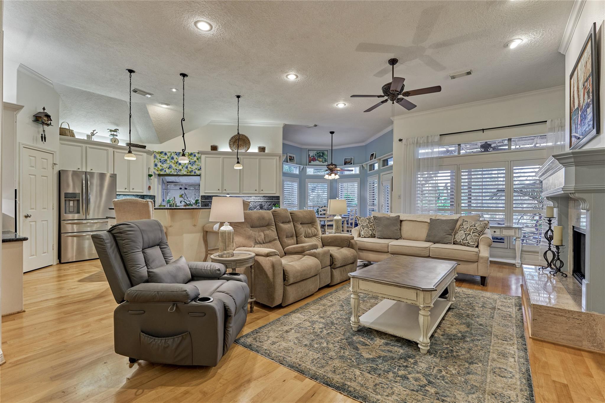 Open-plan living room with recliners, sectional sofa, hardwood floors, and adjoining white kitchen.