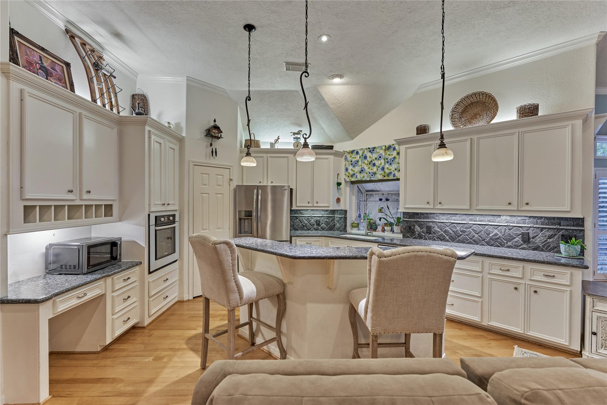 Kitchen with cream cabinets, patterned tile backsplash, stainless appliances, and granite island with two bar stools.