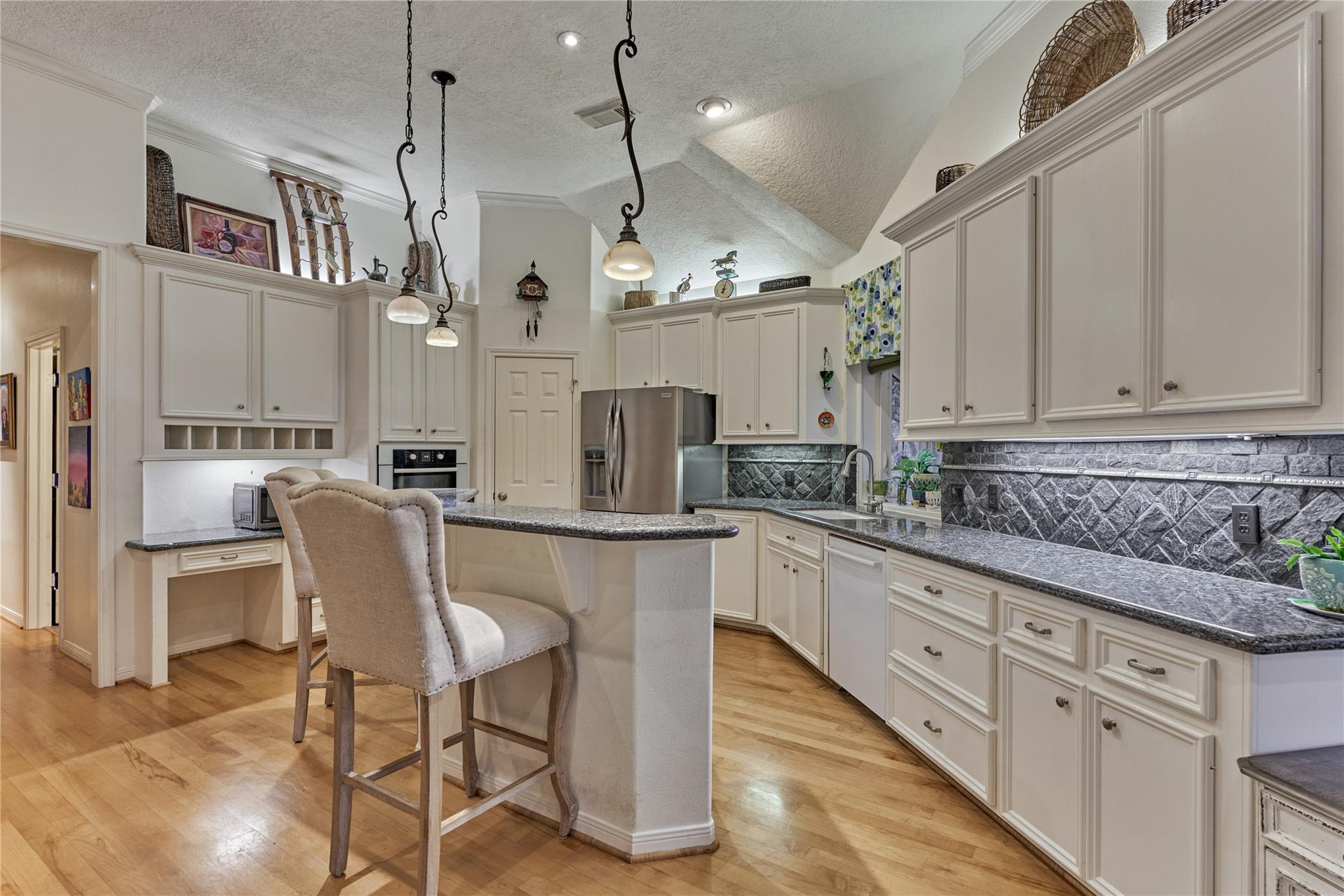 Kitchen with white cabinetry, granite counters, island seating, and a dark stone backsplash.