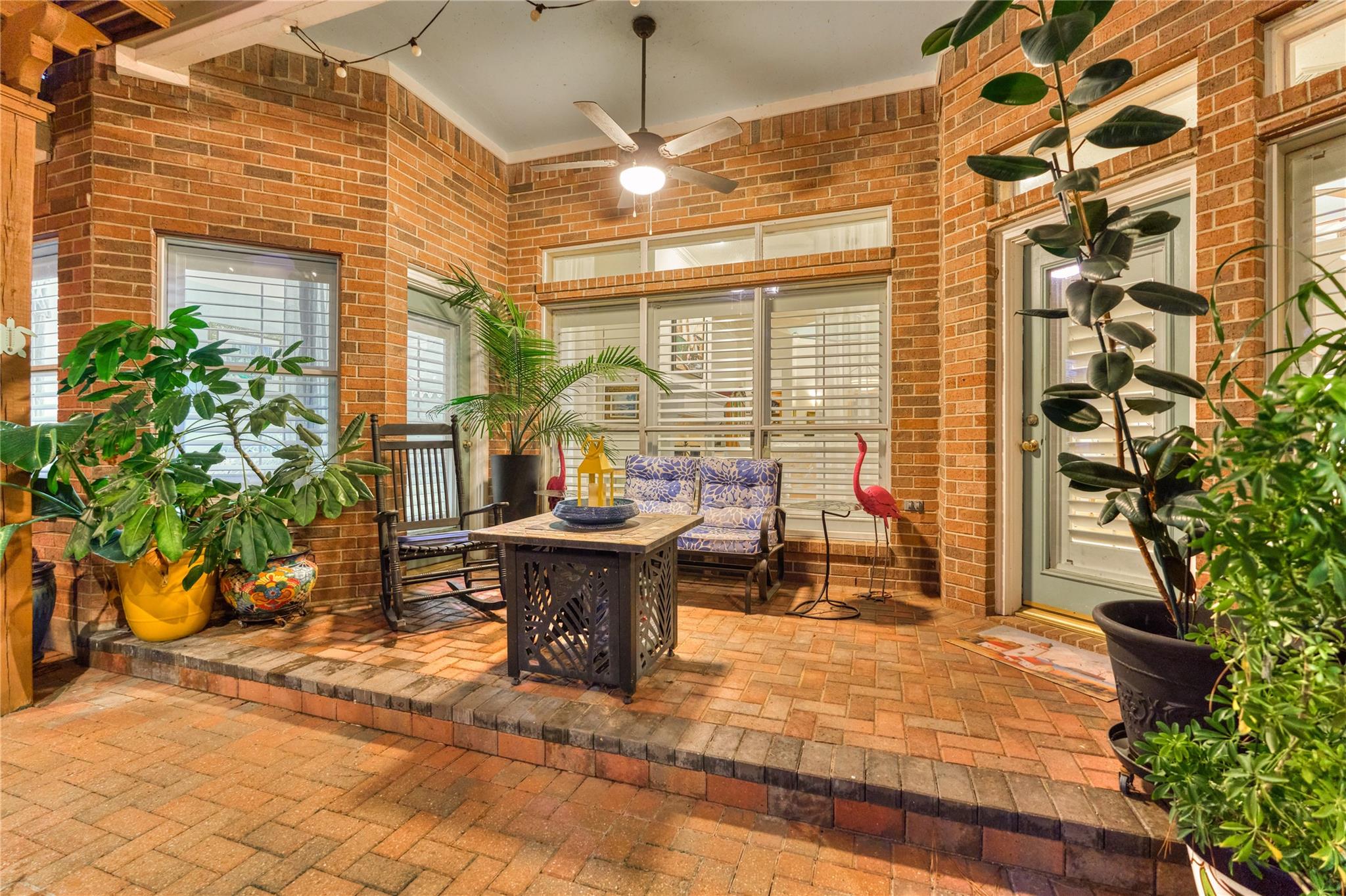 Brick sunroom with shuttered windows, potted plants, and a small seating area.