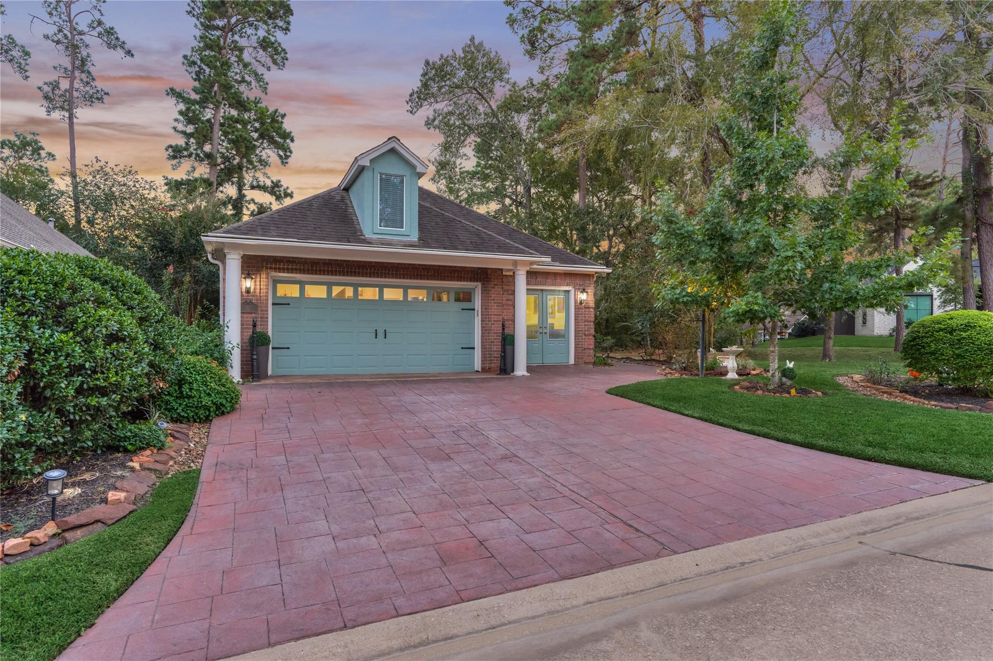 Brick house with a pale blue double garage door and broad stamped-brick driveway at dusk.