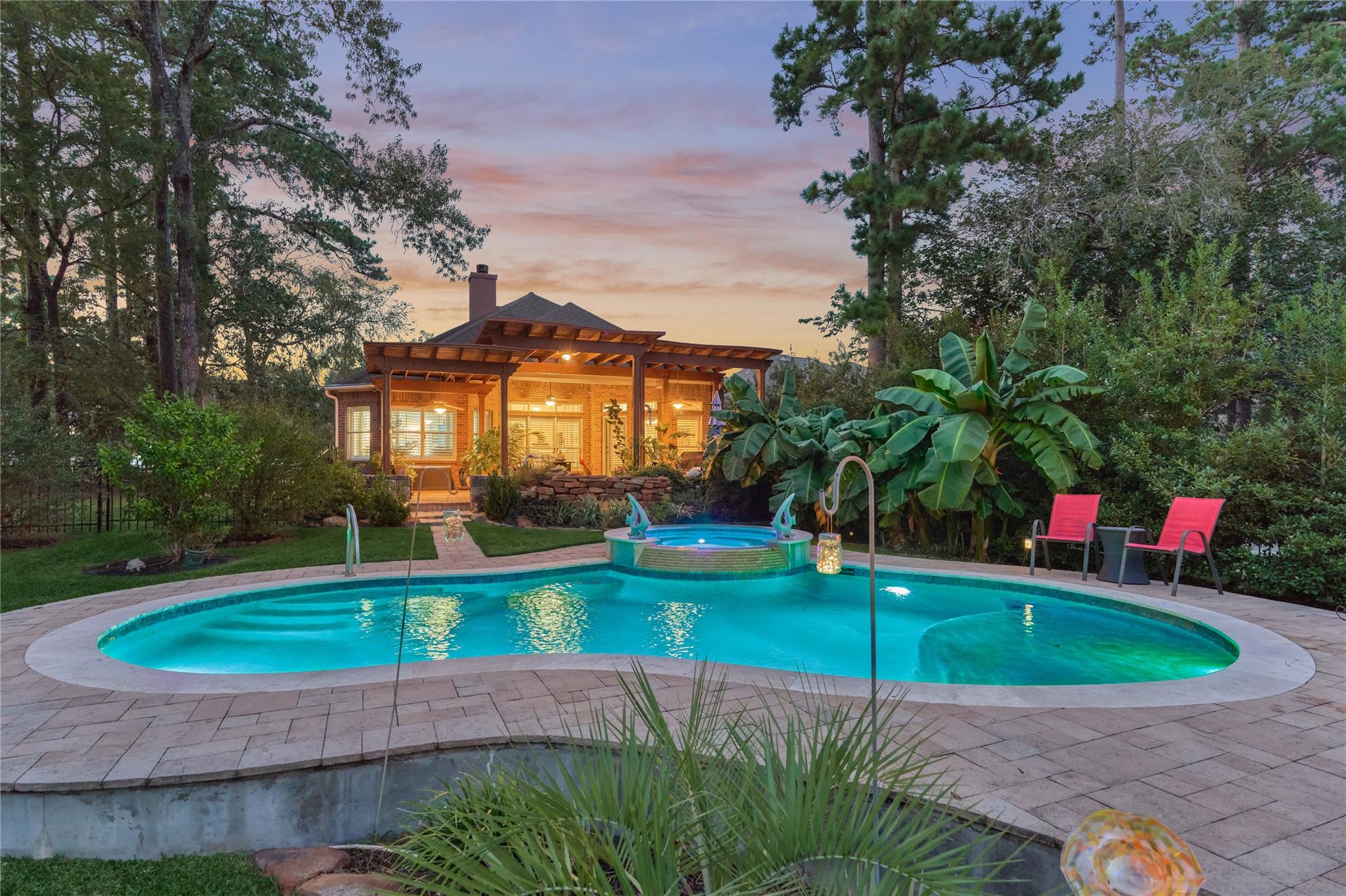 Backyard pool and raised spa in front of a warmly lit home at dusk.
