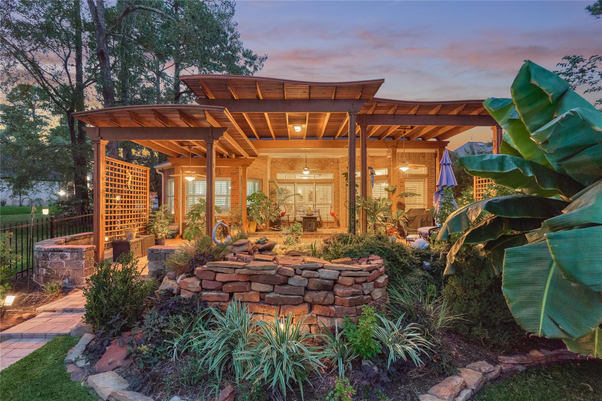 Landscaped brick patio beneath a broad timber pergola, with stone garden walls and lush planting.