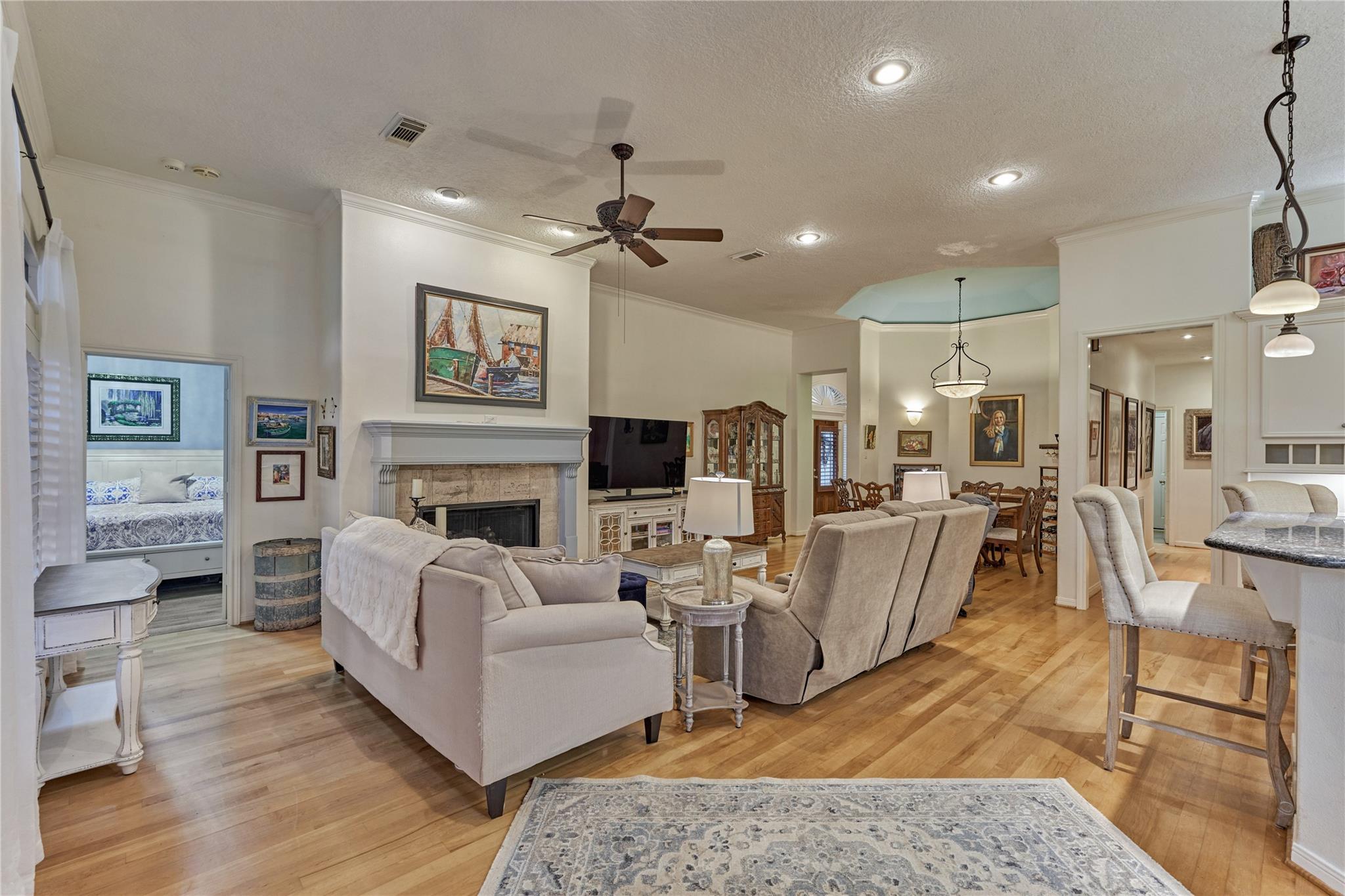 Open-plan living room with light sofas, hardwood floors, and a fireplace opening to the dining area.