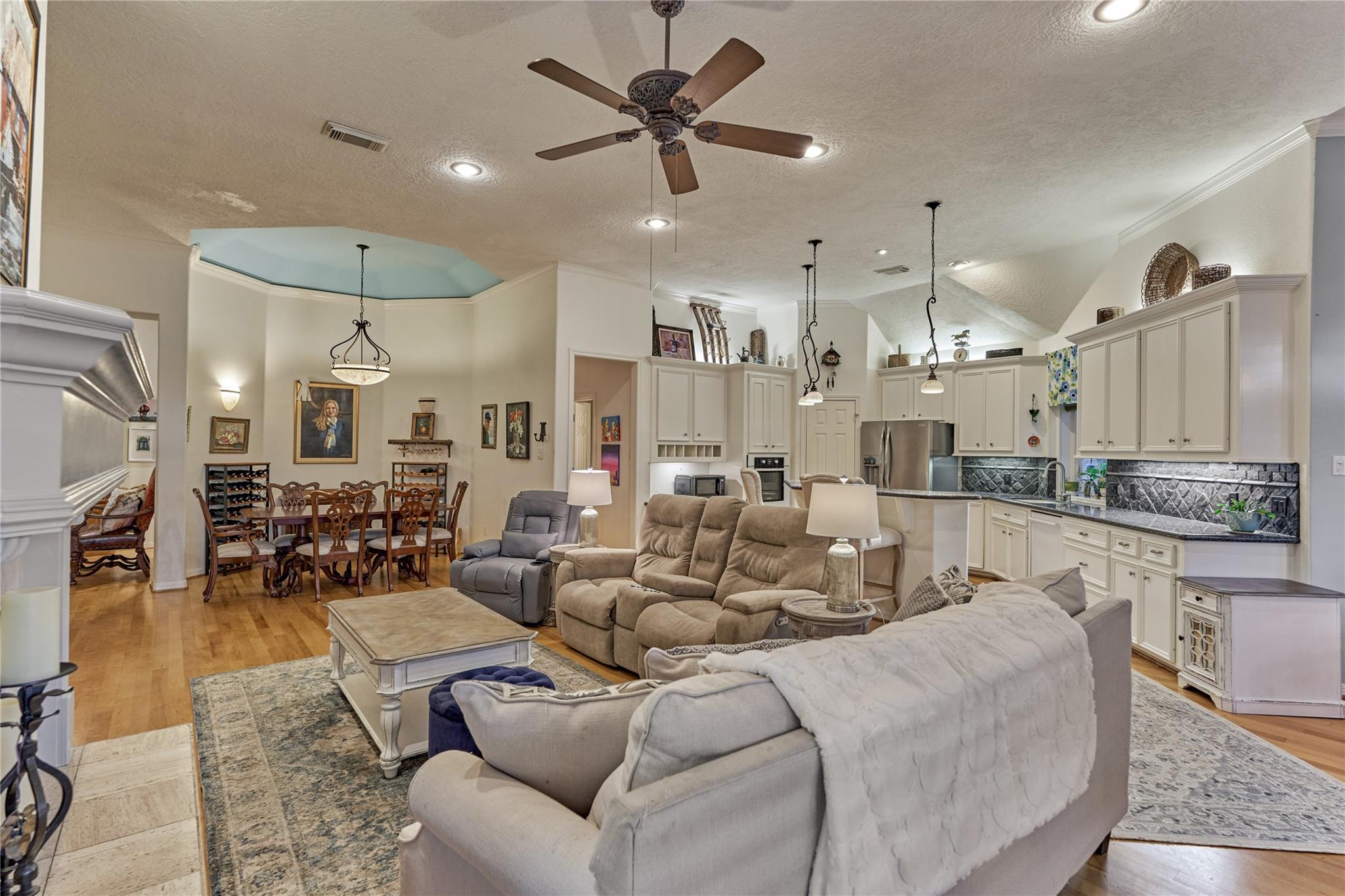 Open living area with dining space and white kitchen, wood floors, and a large ceiling fan.
