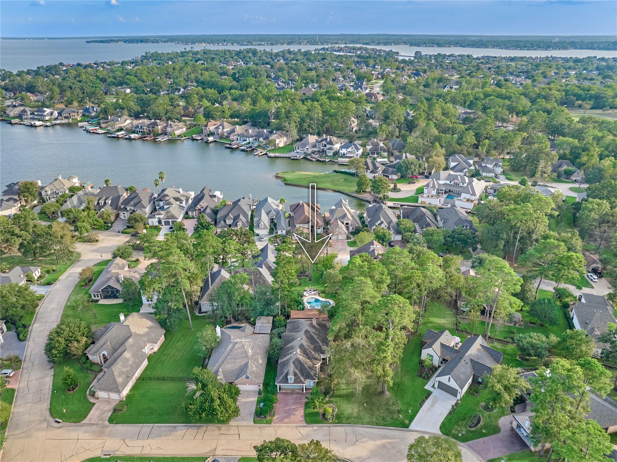 Aerial view of 32 Hillwood Lane marked by an arrow among wooded homes beside a lake.