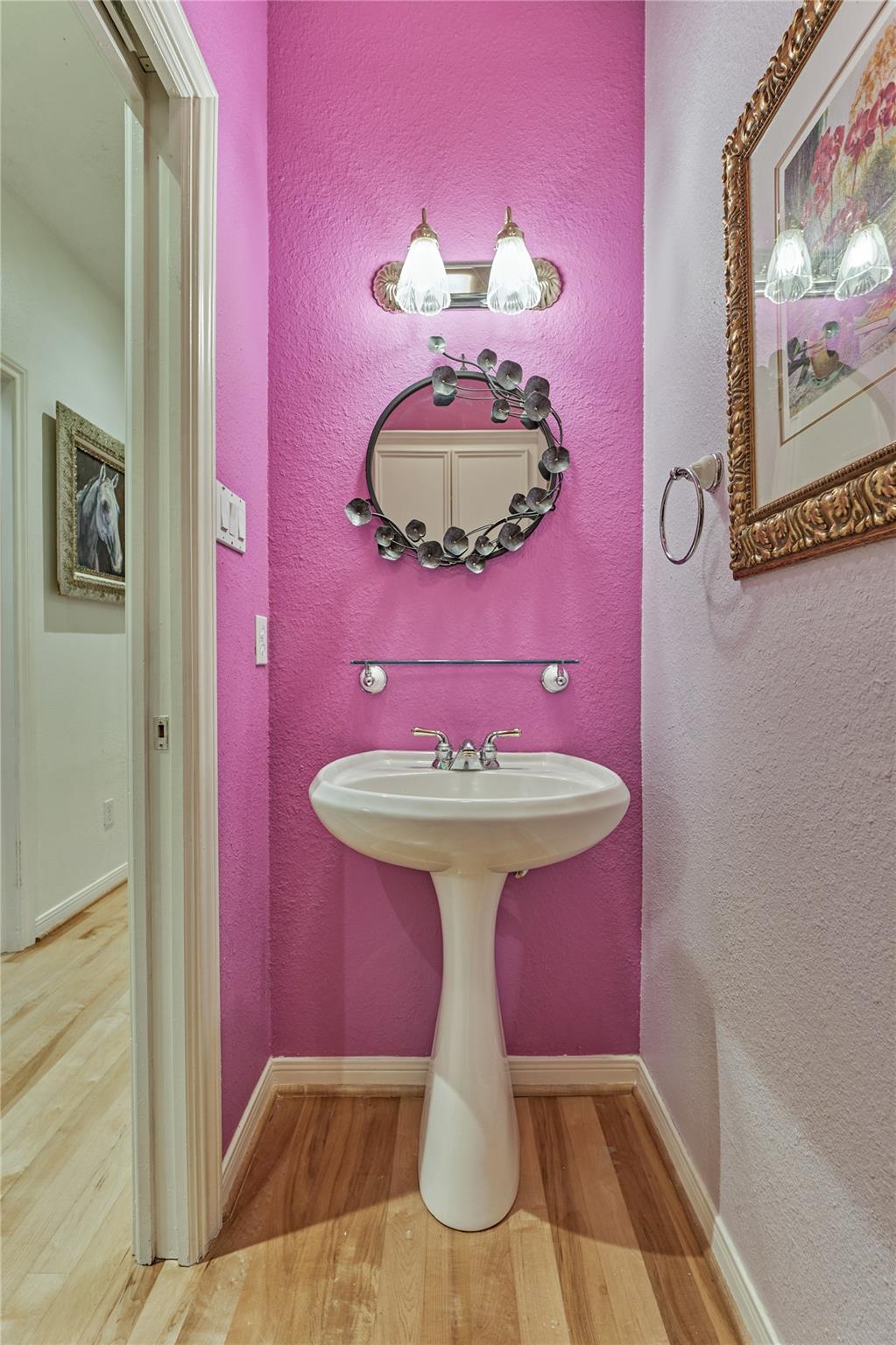 Bathroom with a white pedestal sink, vivid pink walls, and an oval decorative mirror.