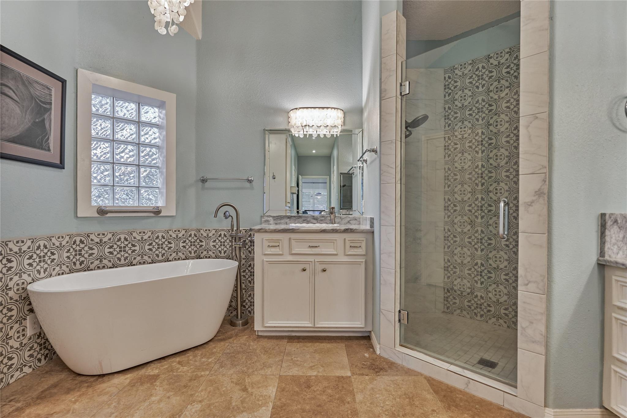 Bathroom with a freestanding soaking tub and glass shower featuring patterned tile.