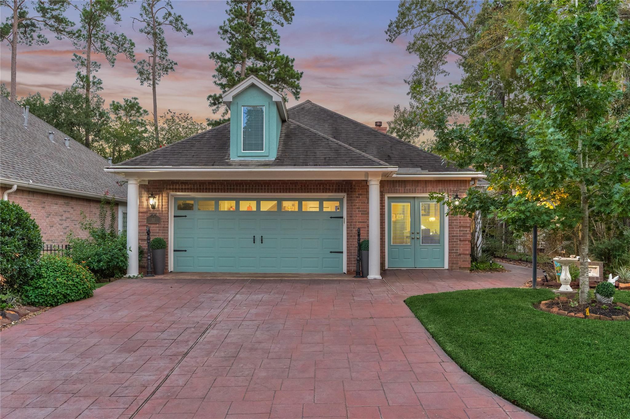 Brick home with a turquoise garage door and entry, red paver driveway, and mature trees at dusk.