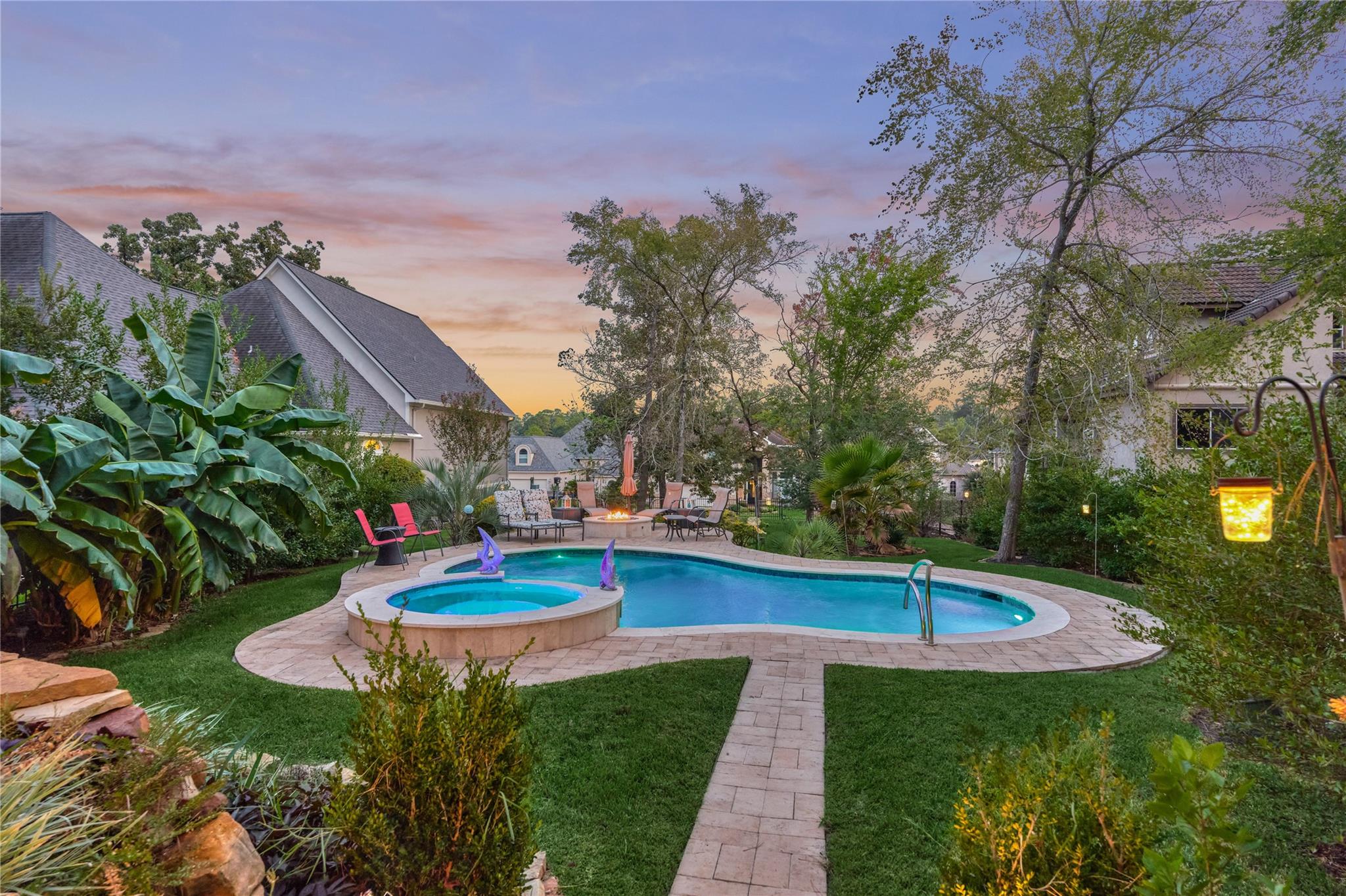 Backyard pool and raised spa with a stone patio and lush landscaping at dusk.