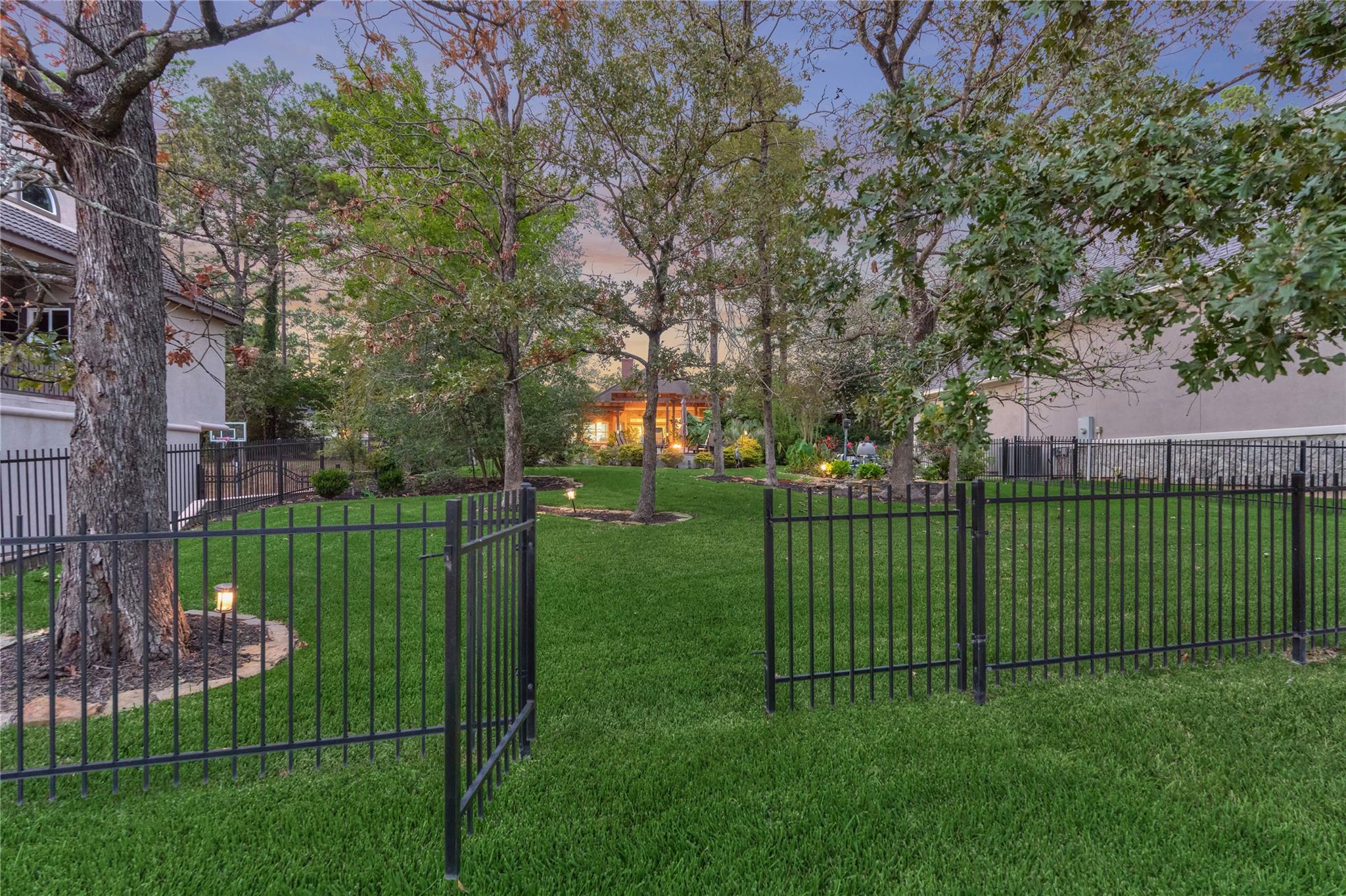 Landscaped backyard with a black metal gate, mature trees, and a glimpse of water.