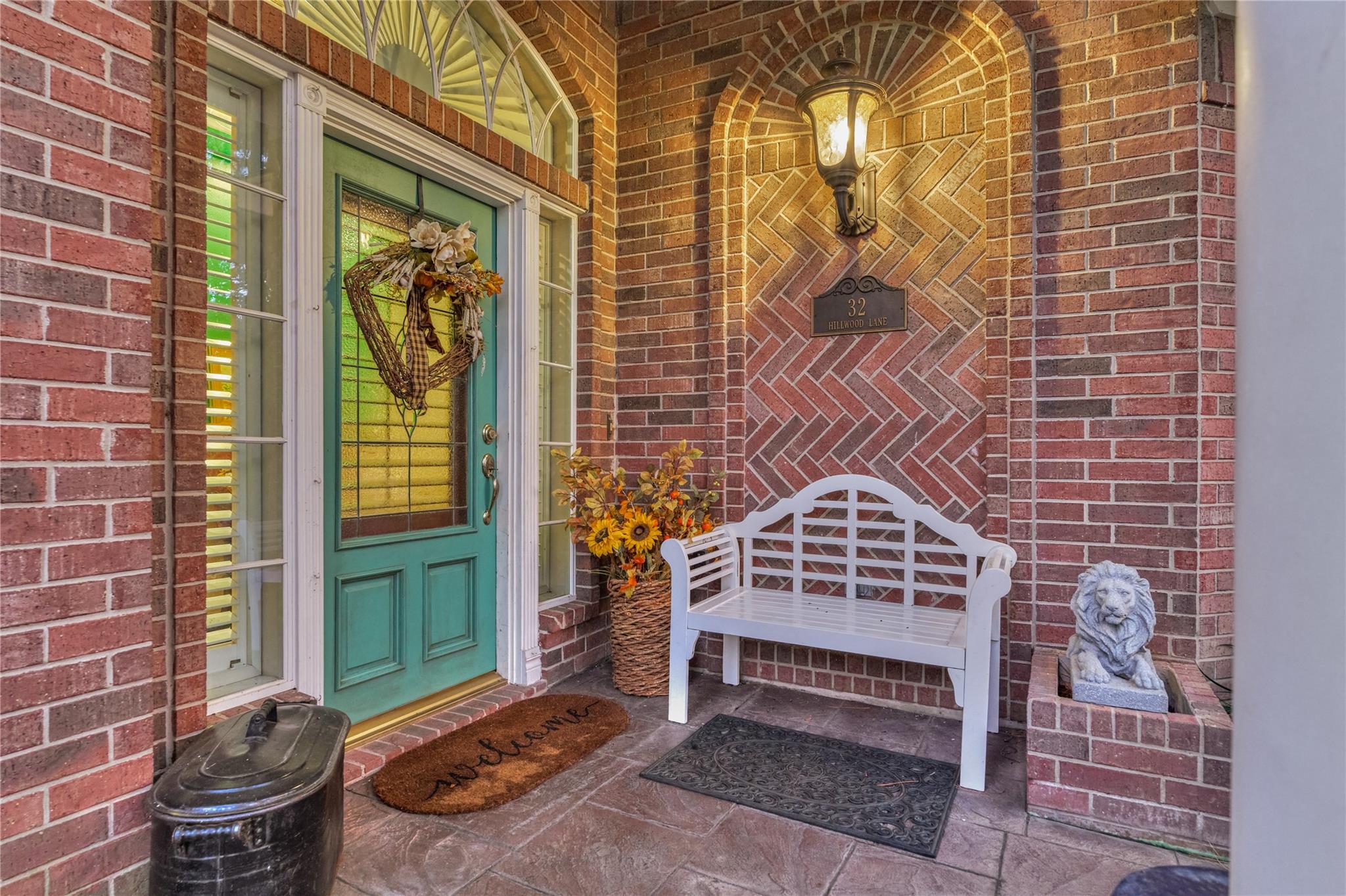 Brick front entry with a teal door, white bench, and 32 Hillwood Lane address plaque.
