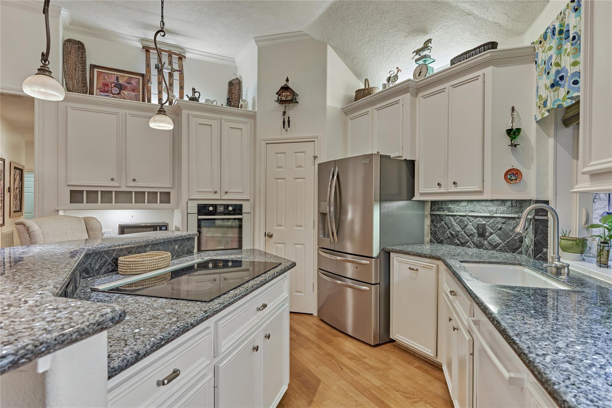 Kitchen with white cabinets, granite counters, stainless steel appliances, and a central cooktop.