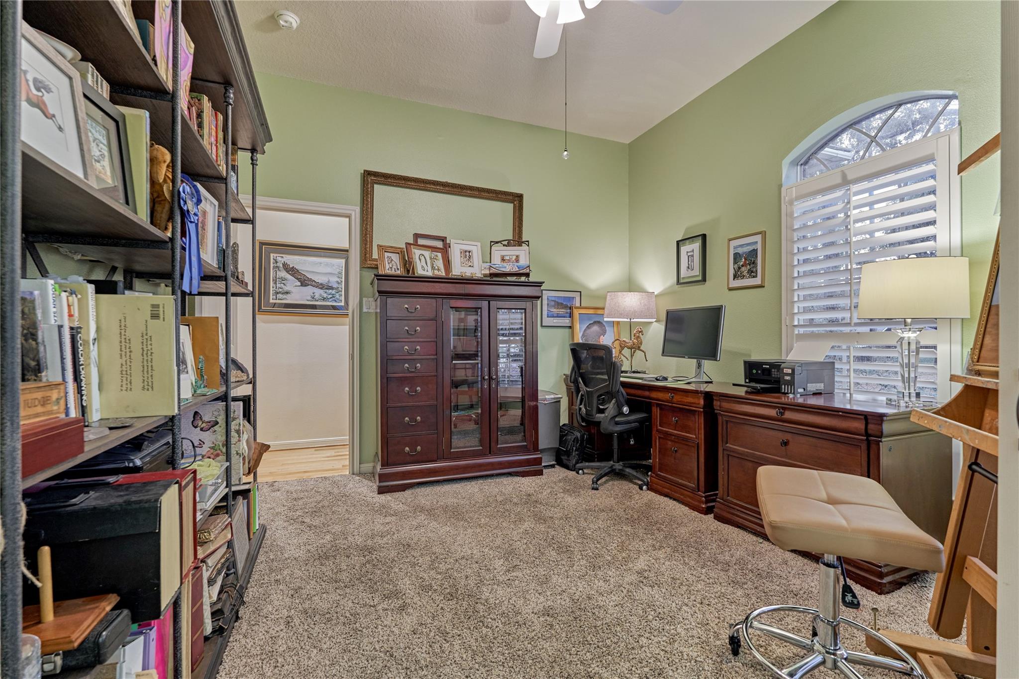 Home office with built-in bookshelves, dark wood desks, and a large arched shuttered window.