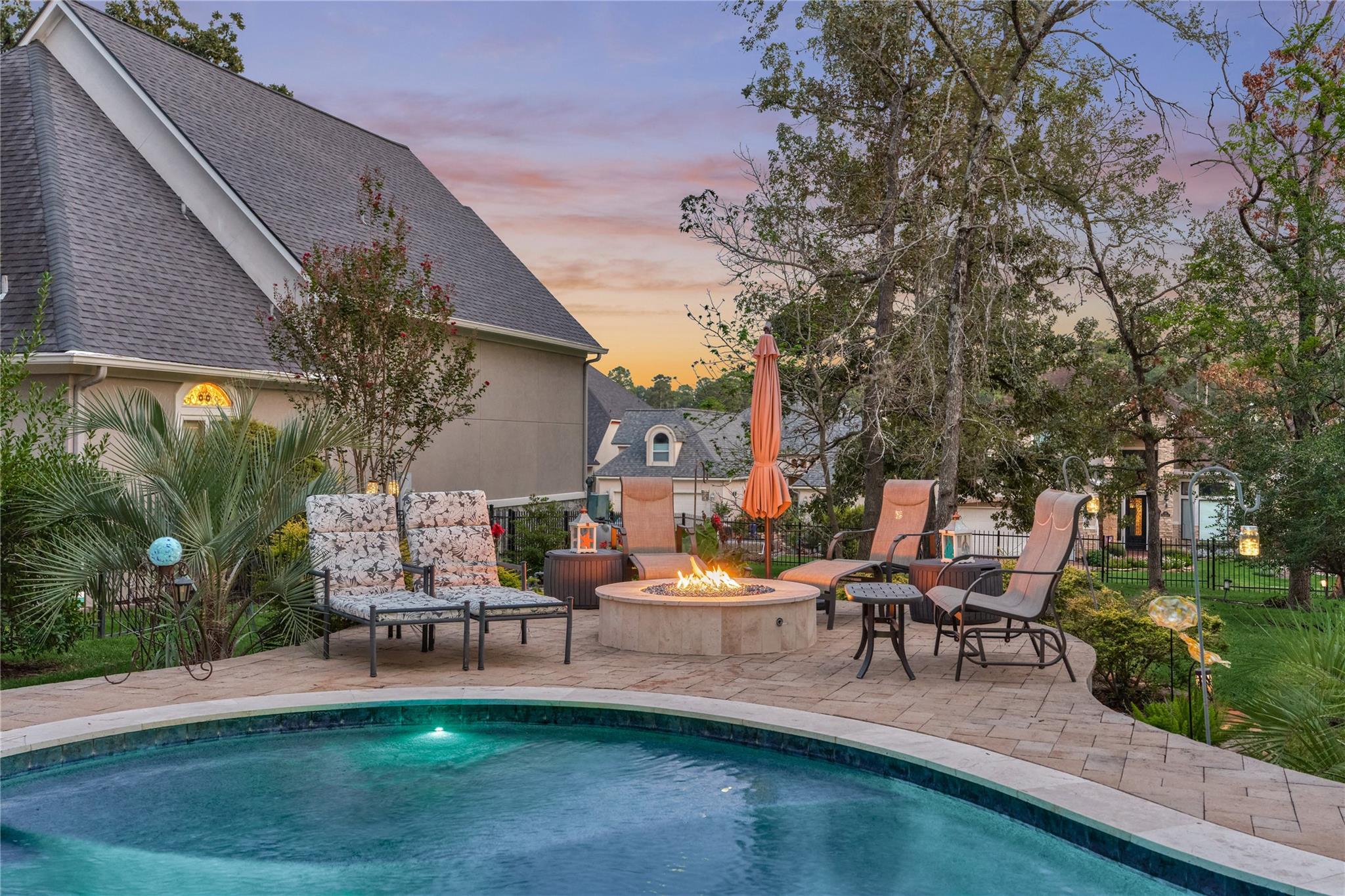 Backyard pool and patio with cushioned seating and a lit fire pit at dusk.