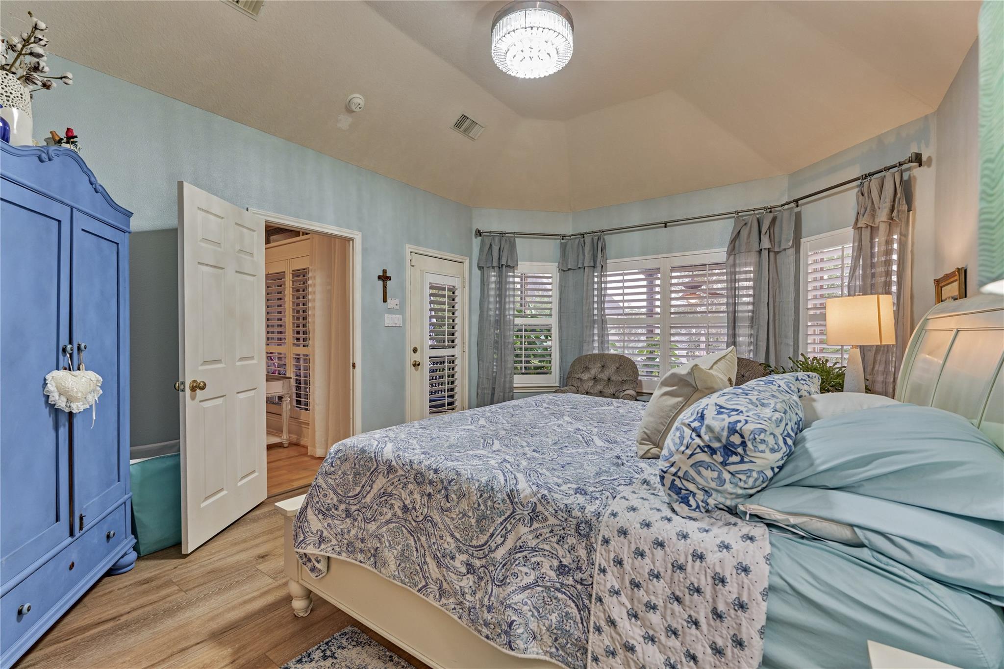 Bedroom with blue-and-white bedding, a blue armoire, and shuttered bay windows.