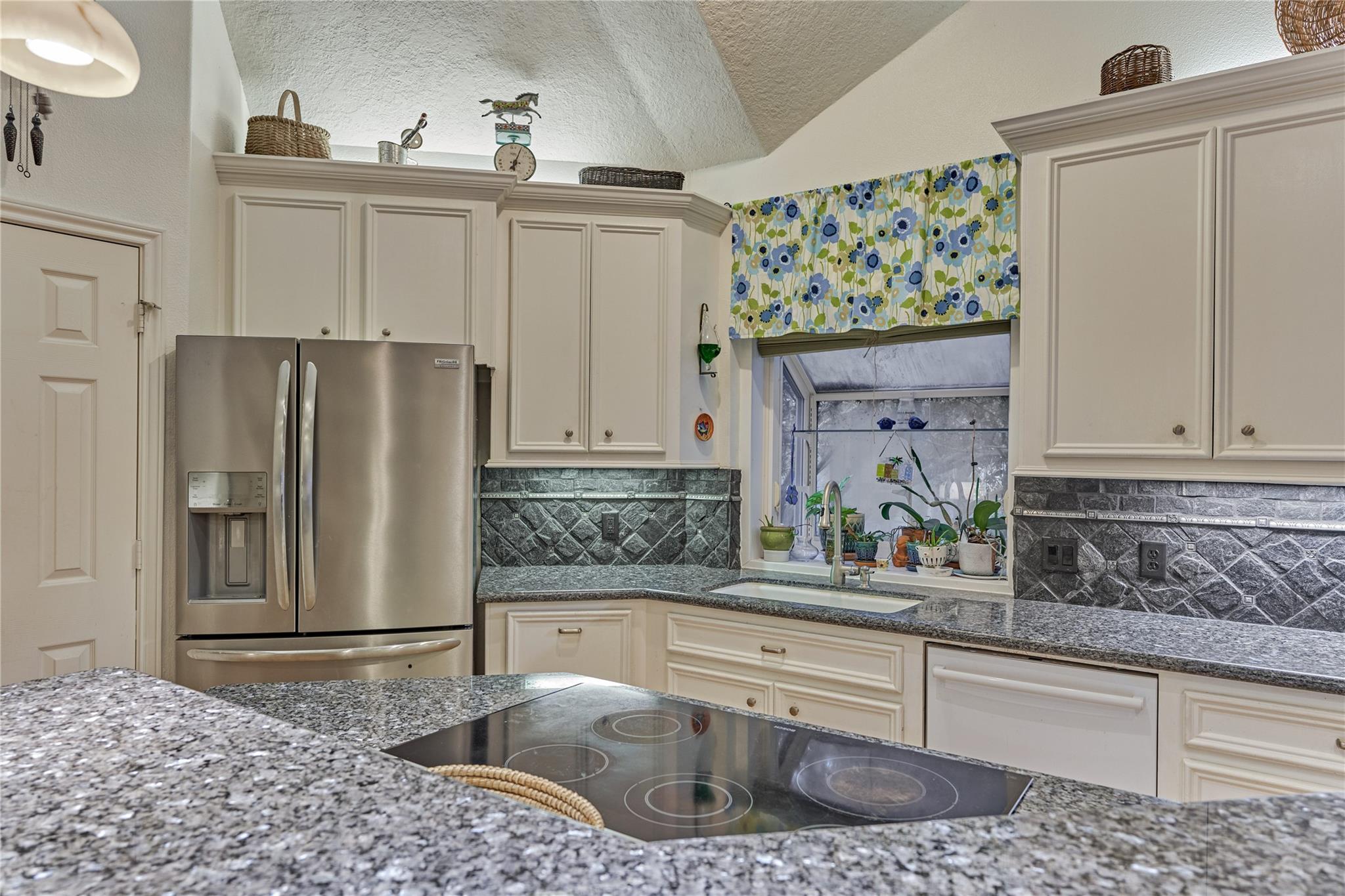Kitchen with cream cabinets, granite counters, stainless steel refrigerator, and a cooktop island.