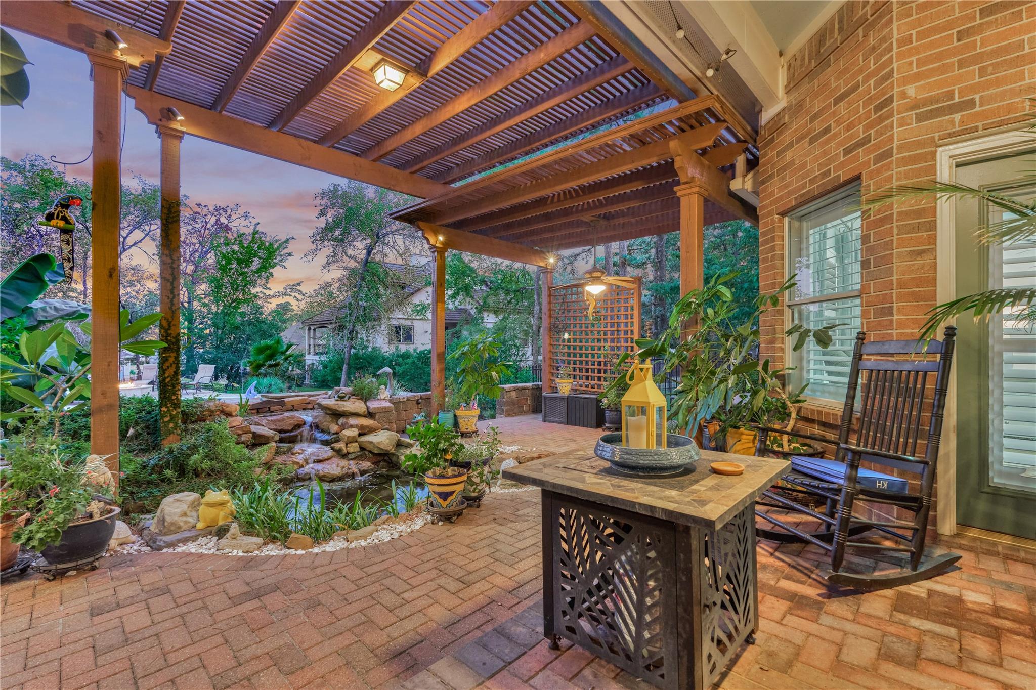 Covered brick patio with a timber pergola, rocking chairs, and a garden water feature.