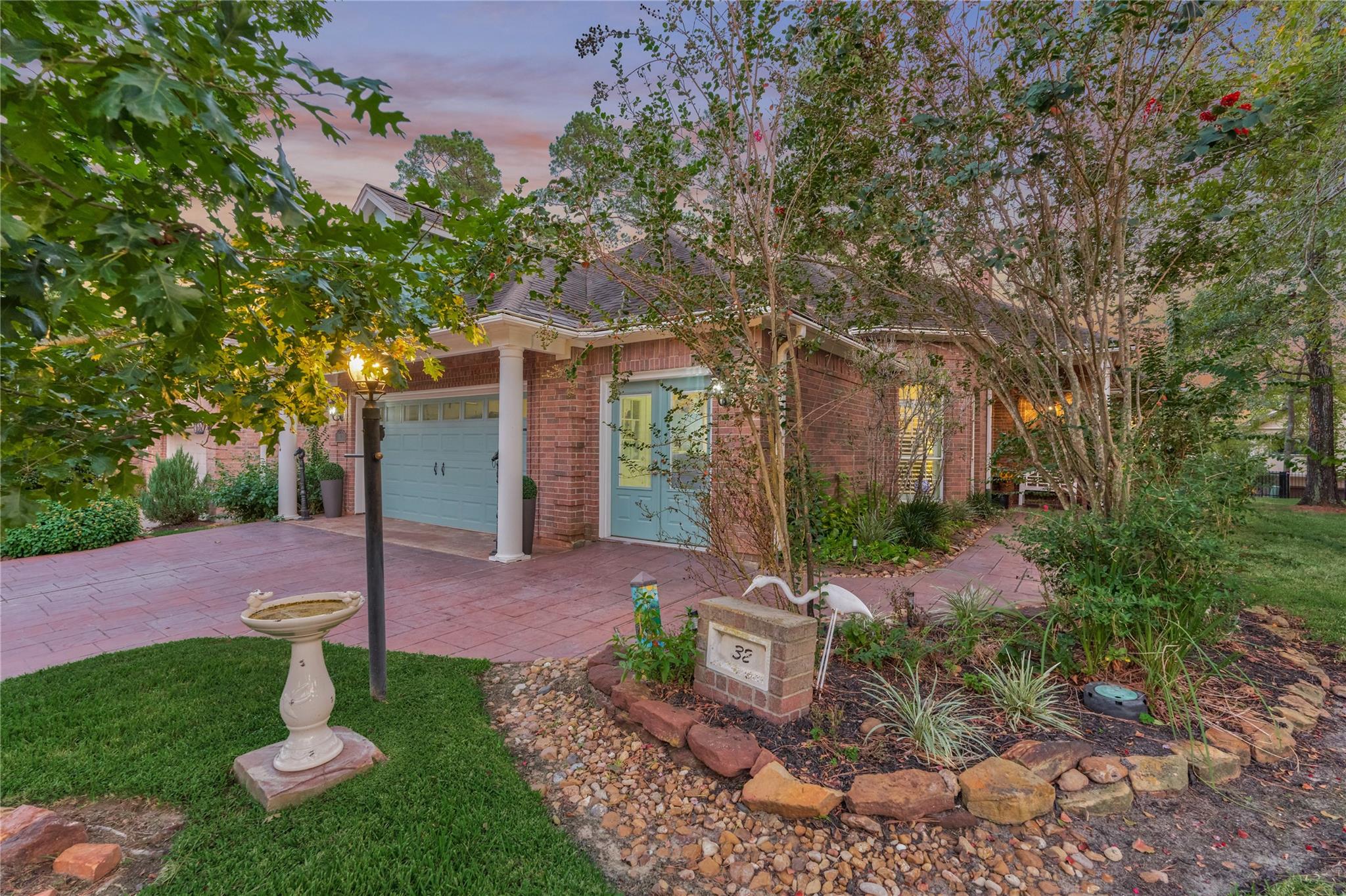 Red-brick home with blue-gray doors, landscaped stone beds, and a birdbath at sunset.