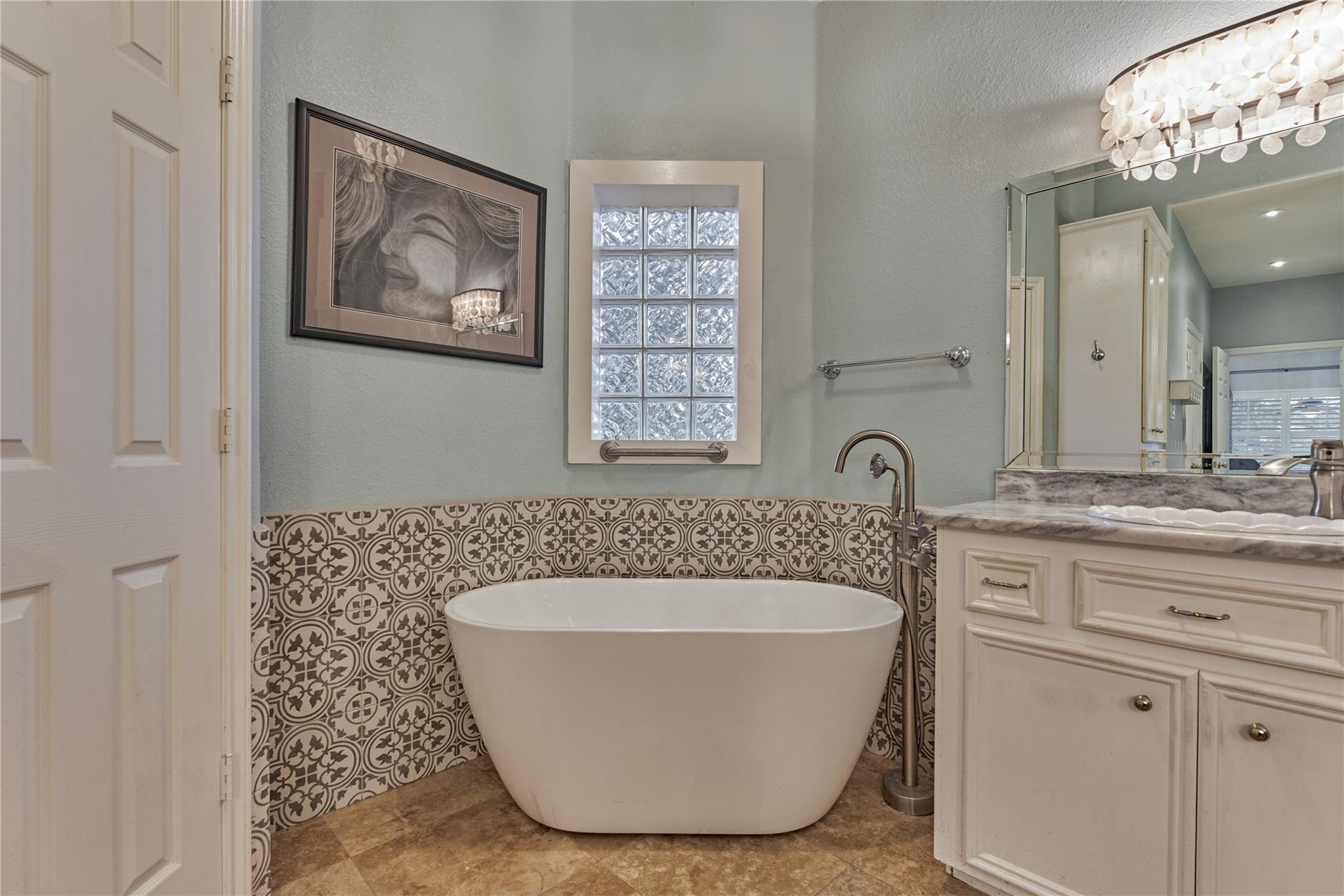 Bathroom with a freestanding tub, patterned tile, glass-block window, and cream vanity.