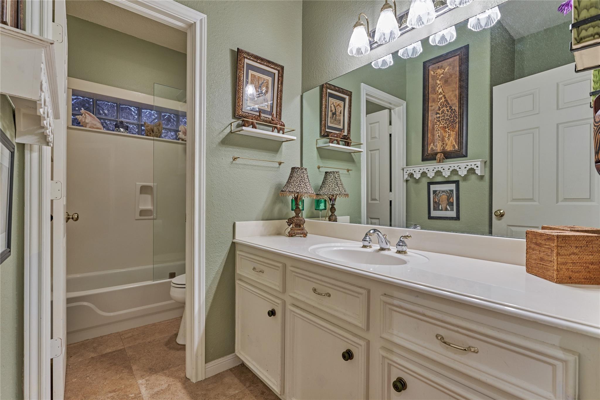 Bathroom with cream vanity and large mirror beside a glass-enclosed tub and shower.