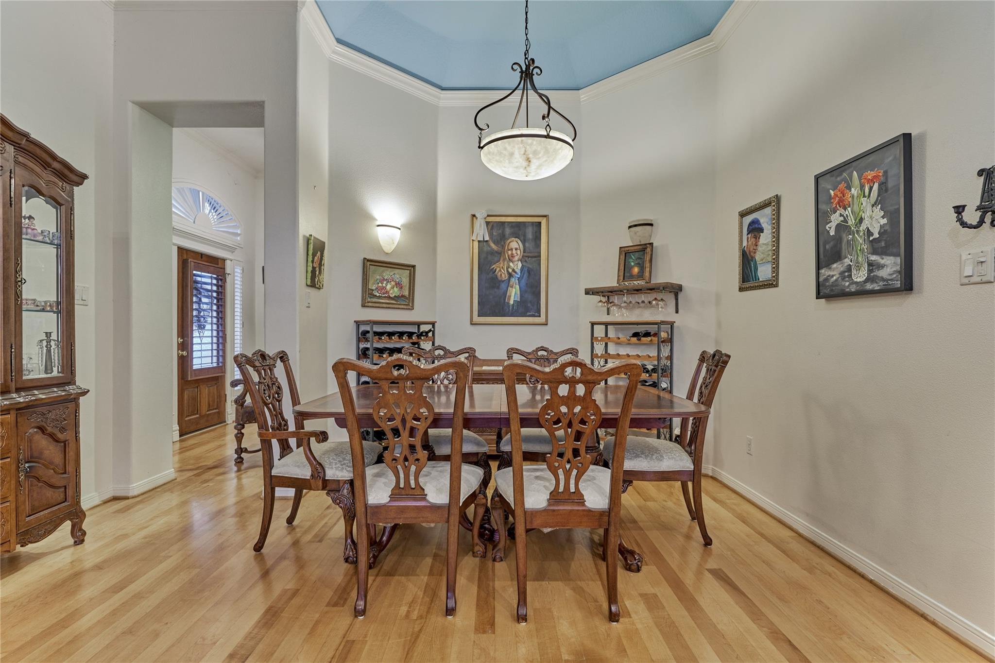 Dining room with a carved wood table and chairs beneath a blue tray ceiling and chandelier.