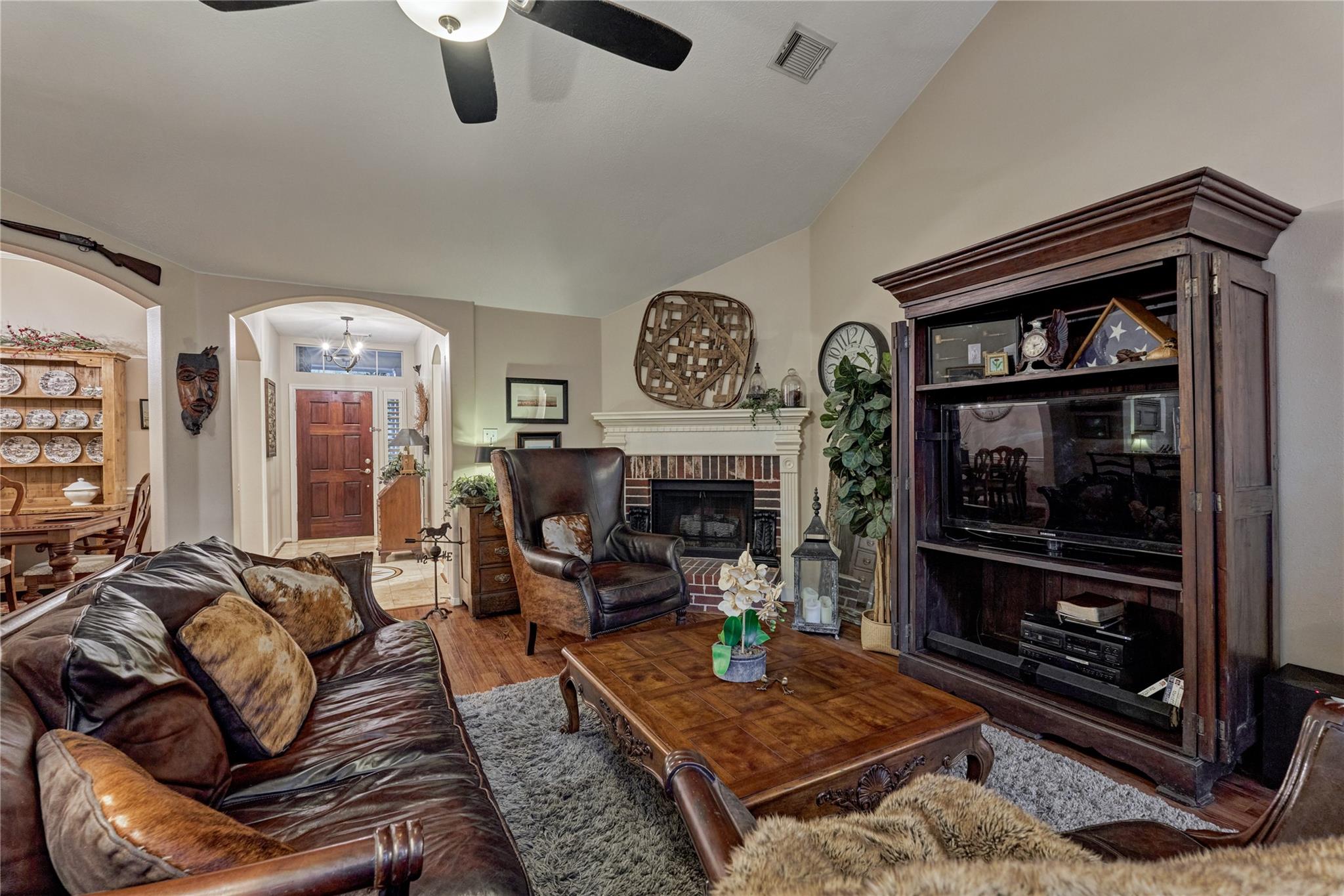 Living room with leather seating, a brick fireplace, and a large dark wood entertainment cabinet.