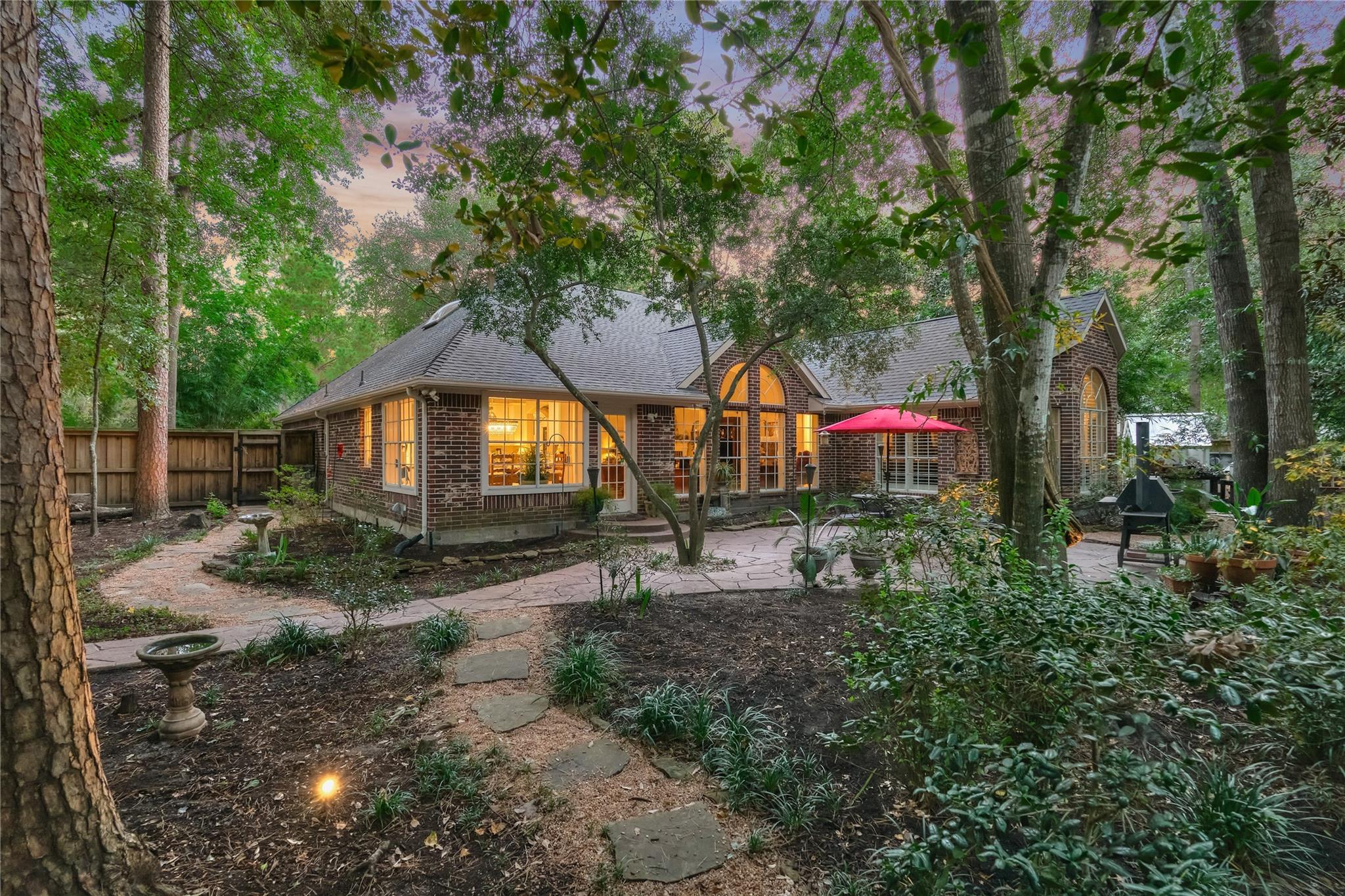 Brick home viewed from a wooded backyard, with a stone patio and red umbrella.