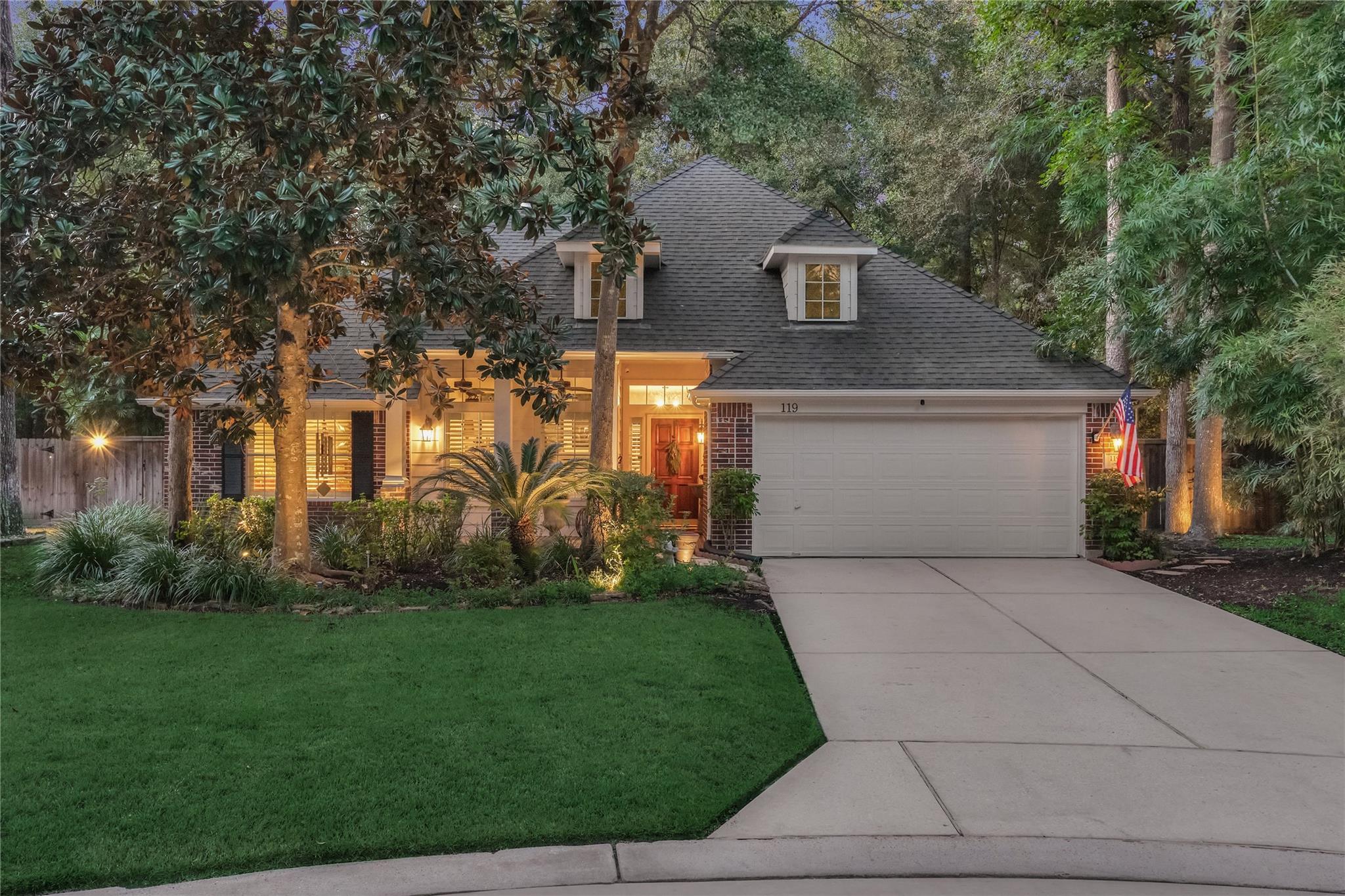 Brick house at dusk with a two-car garage, landscaped front yard, and mature trees.