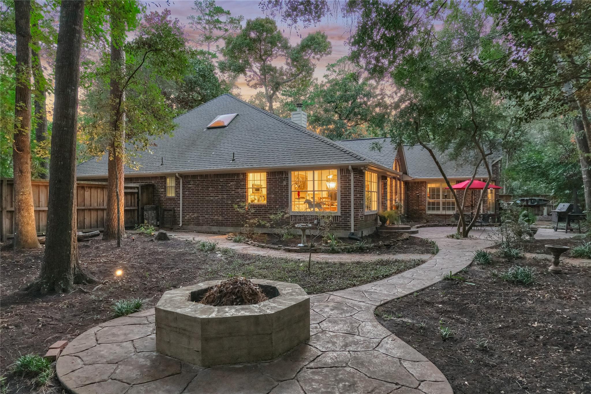 Brick home at dusk with a wooded backyard, curved stone patio, and circular fire pit.