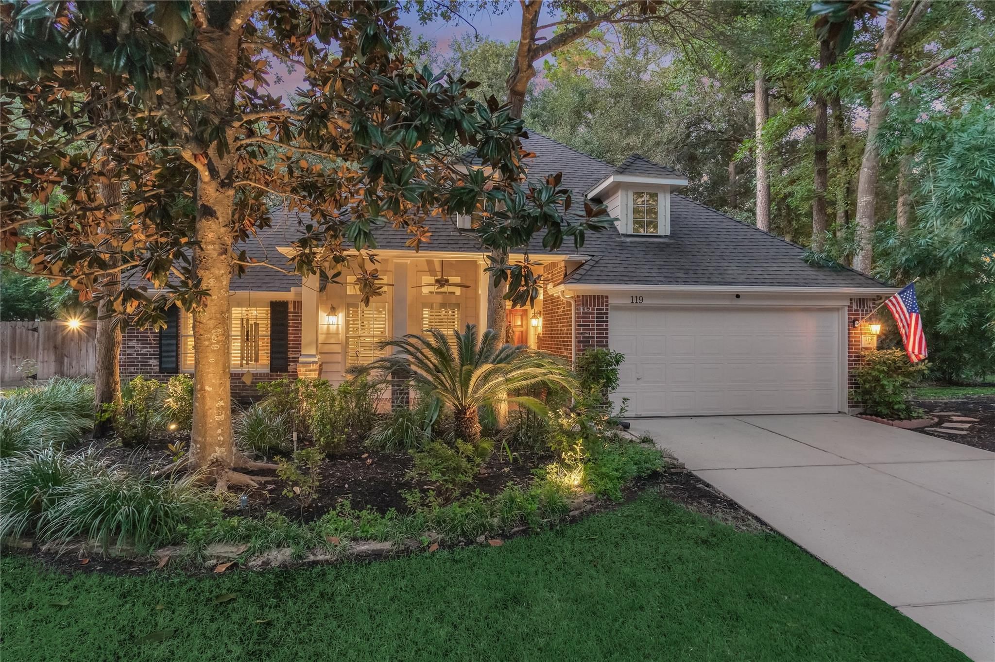 Brick home with a two-car garage, warmly lit entry, and mature trees at dusk.