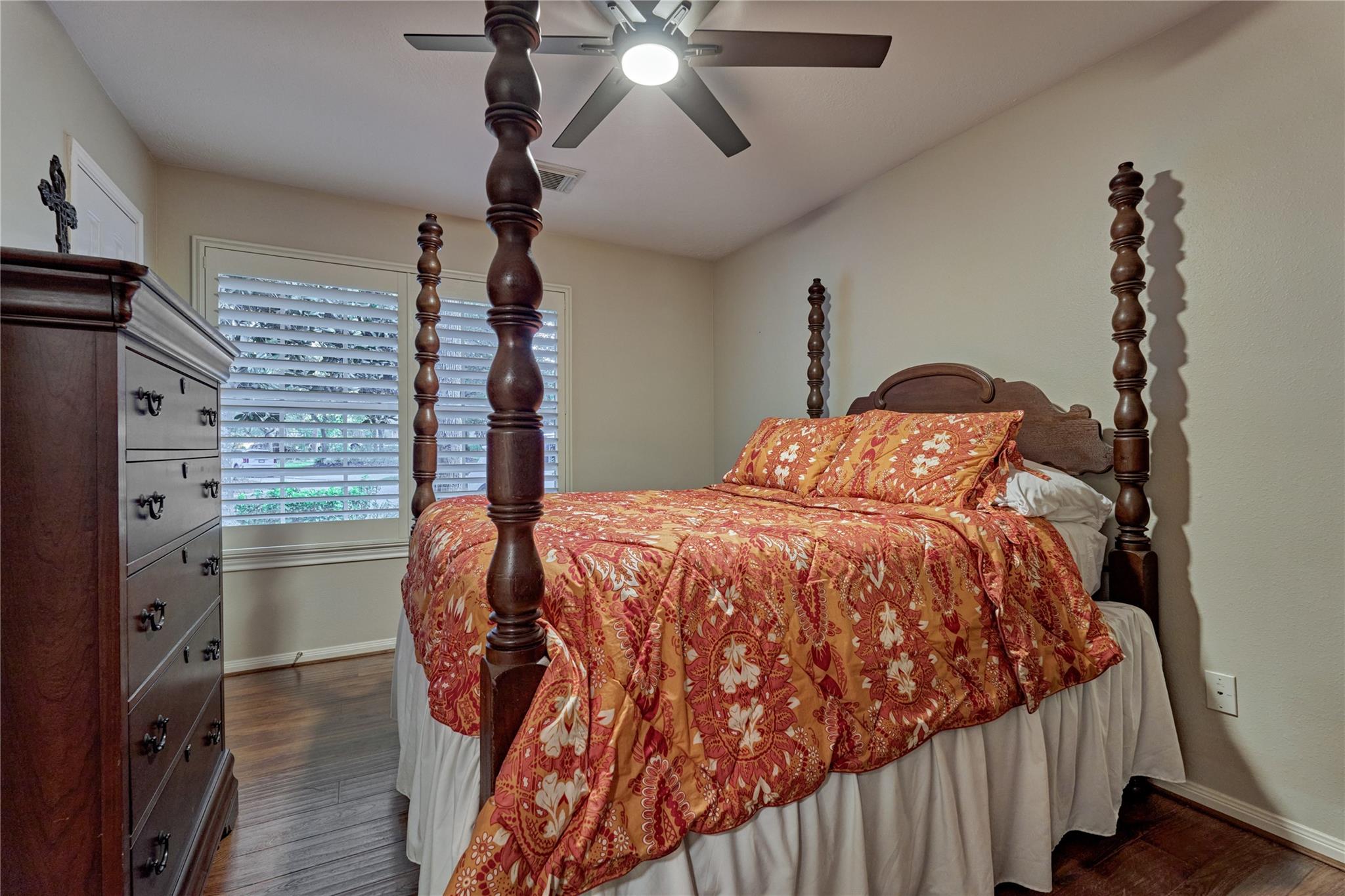 Bedroom with a dark wood four-poster bed and orange floral bedding beside plantation shutters.