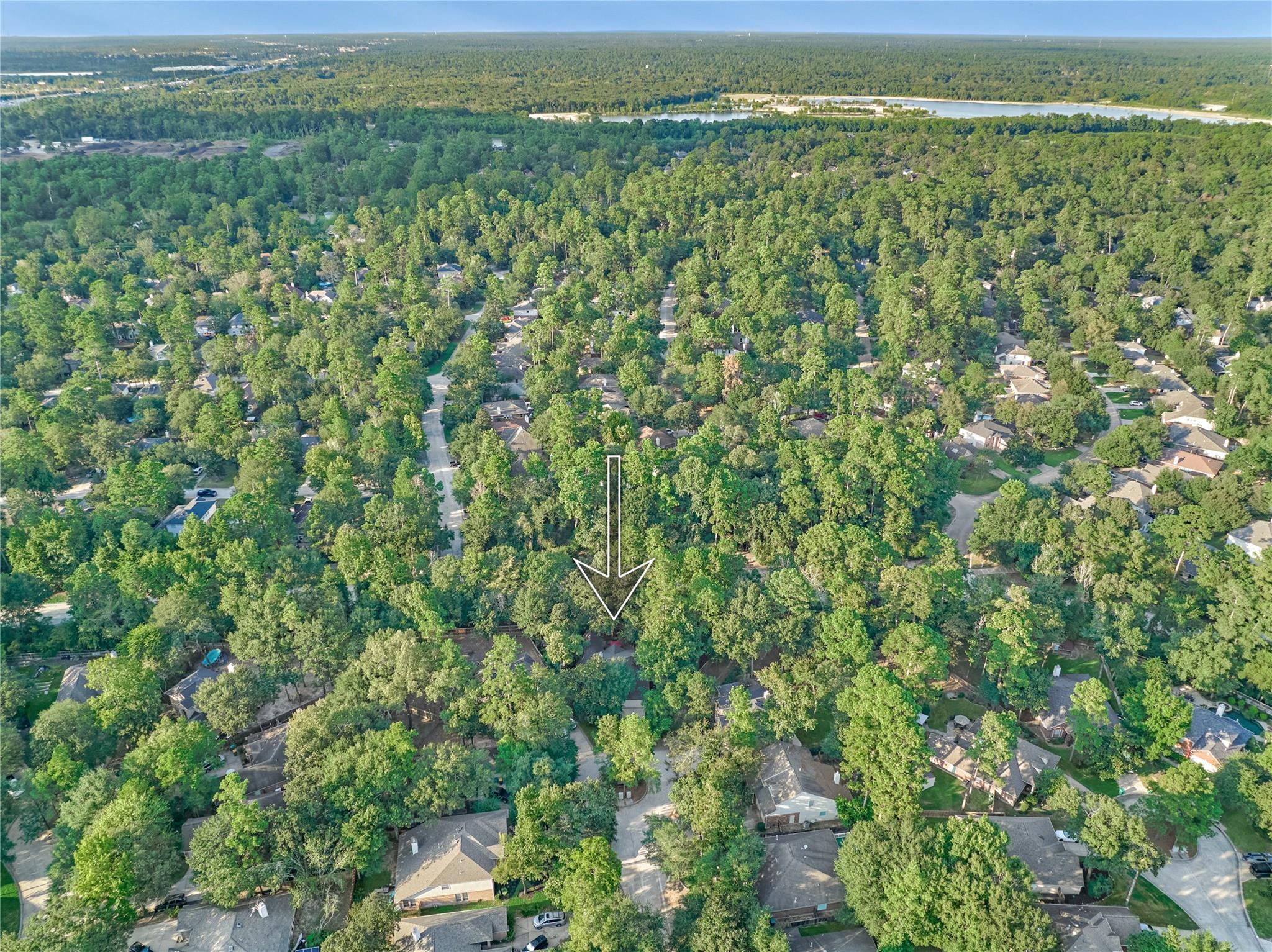 Aerial neighborhood view with an arrow marking the wooded property site.