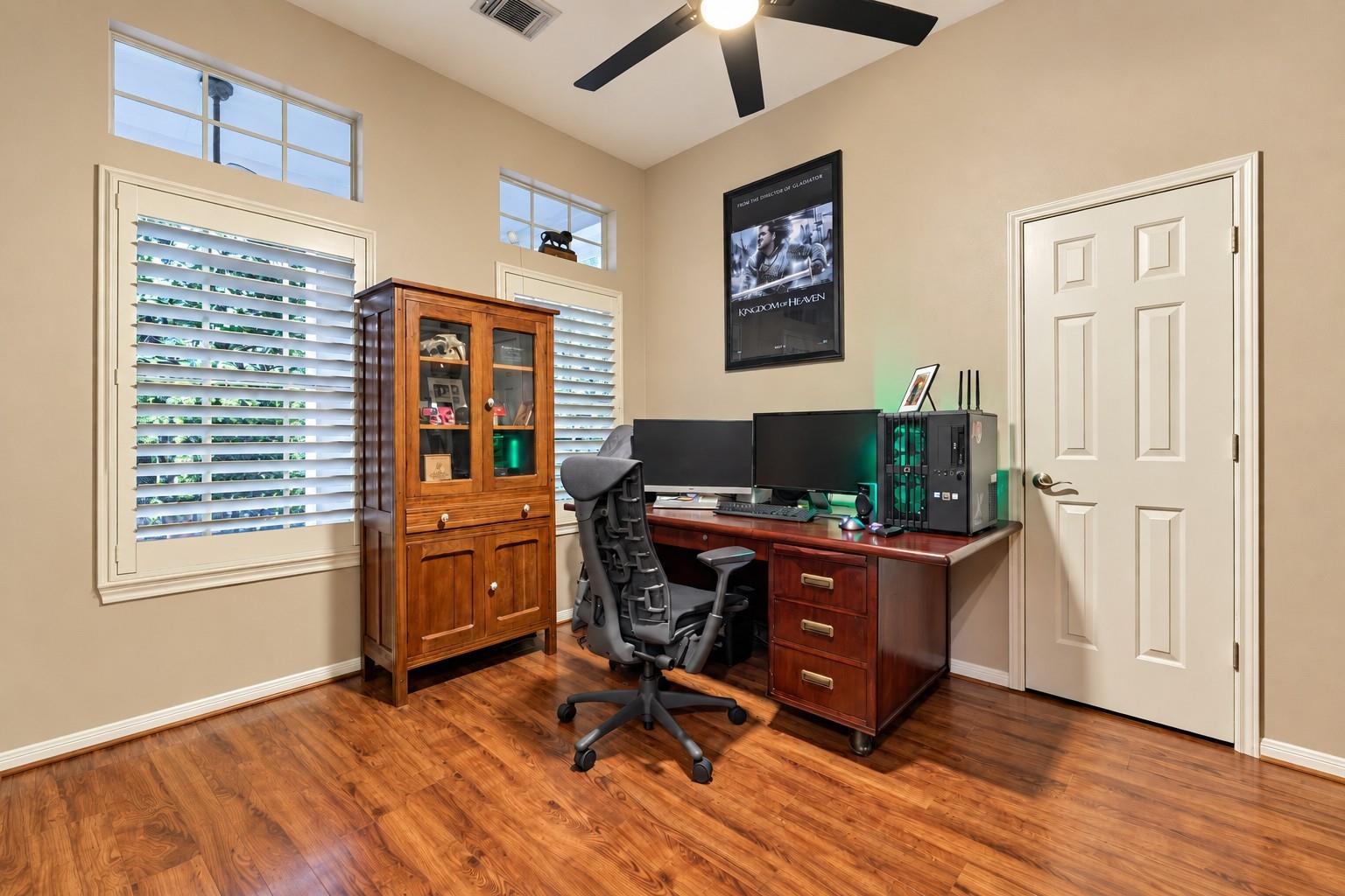 Home office with dual monitors, a wooden desk, and an ergonomic chair on hardwood floors.