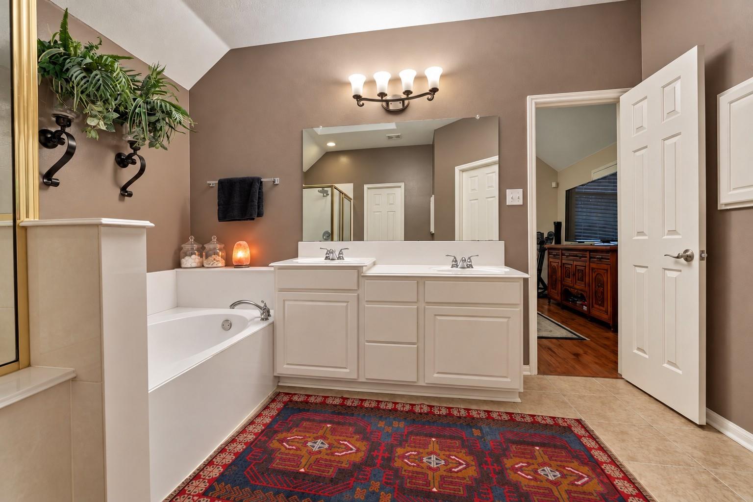 Primary bathroom with a soaking tub, double vanity, large mirror, and patterned rug.