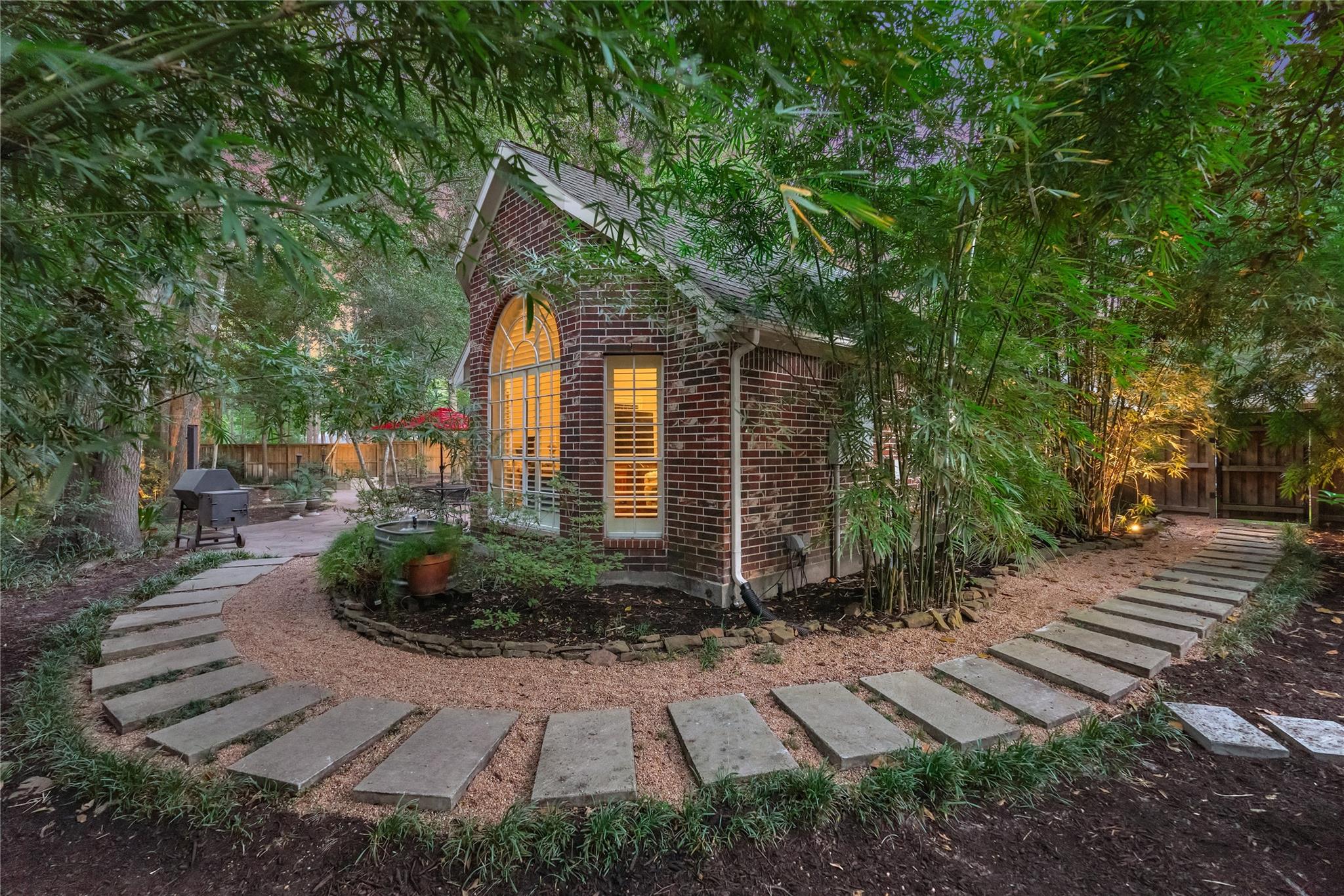 Brick home with glowing arched windows, framed by bamboo and curving backyard stepping-stone paths.