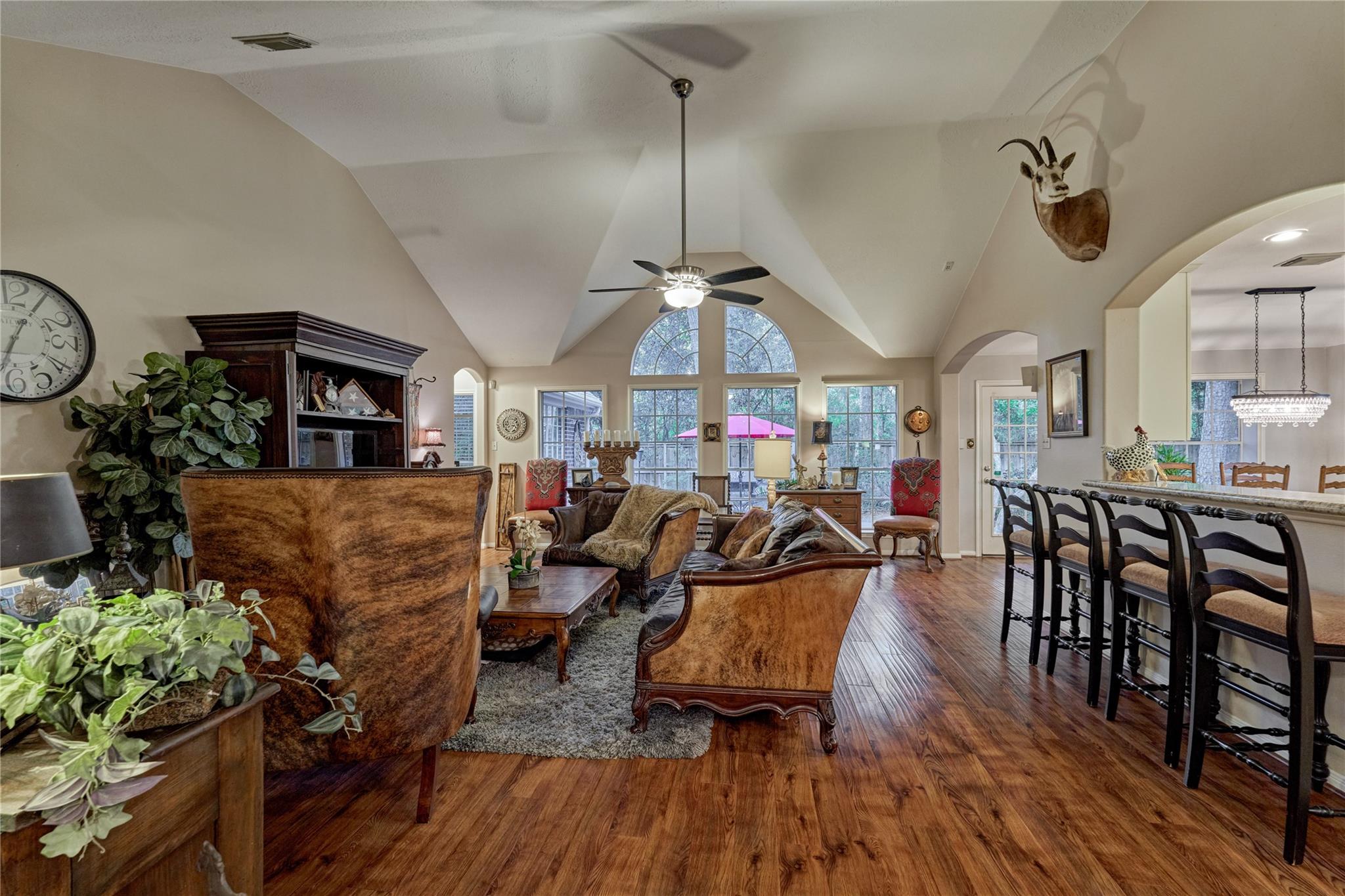 Living room with vaulted ceilings, arched windows, hardwood floors, and an adjoining breakfast bar.